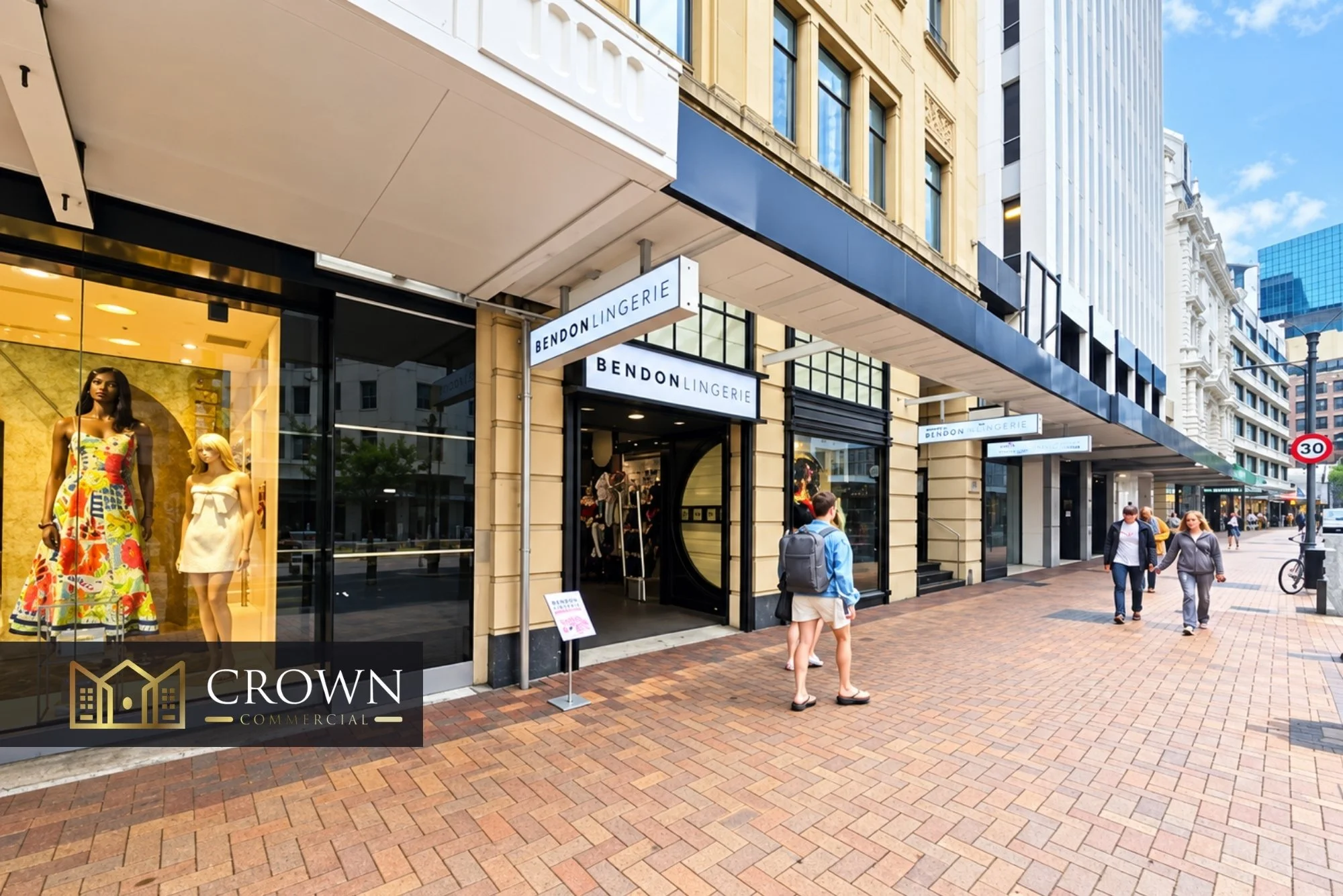 A busy city street scene featuring storefronts, pedestrians, and tall office buildings. One store, Bendon Lingerie, has mannequins displaying colorful and white clothing in the window.