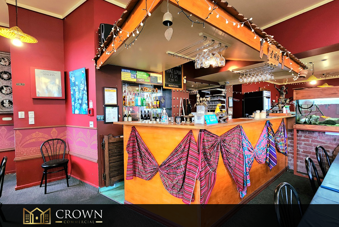 A cozy restaurant interior with red and pink walls, decorated with patterned cloths on the bar, a fish tank, and hanging wine glasses, featuring a small bar area with bottles and glasses.