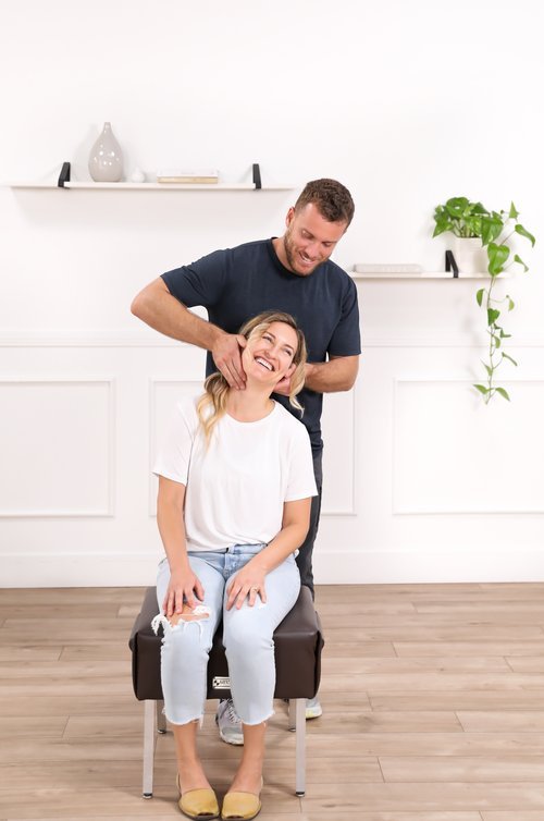 Dr. Yossi Stein preparing to perform a seated cervical adjustment on a smiling patient at Stein Chiropractic in San Diego.
