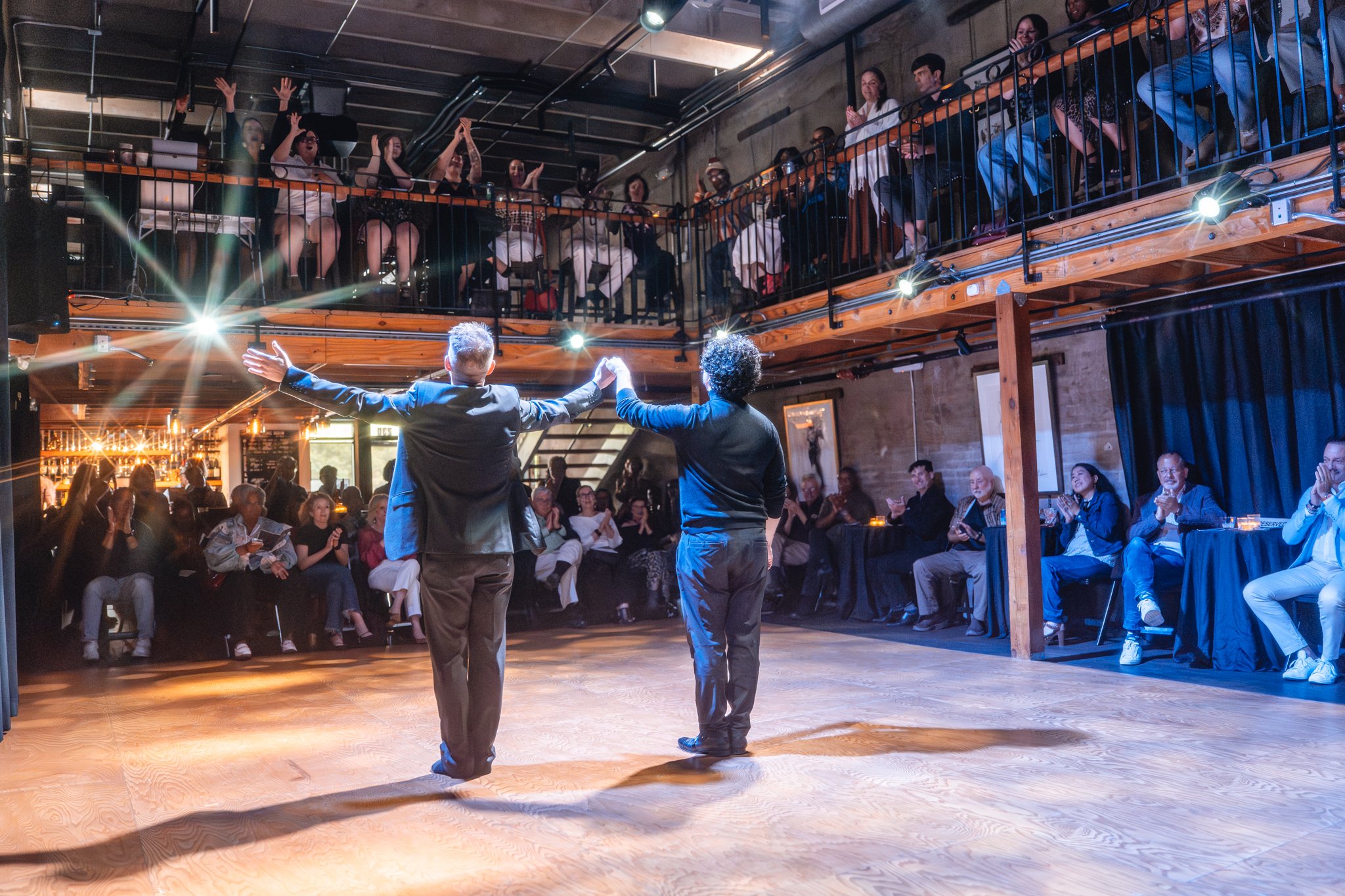 two men taking a bow on stage at The Long Room with full audience clapping