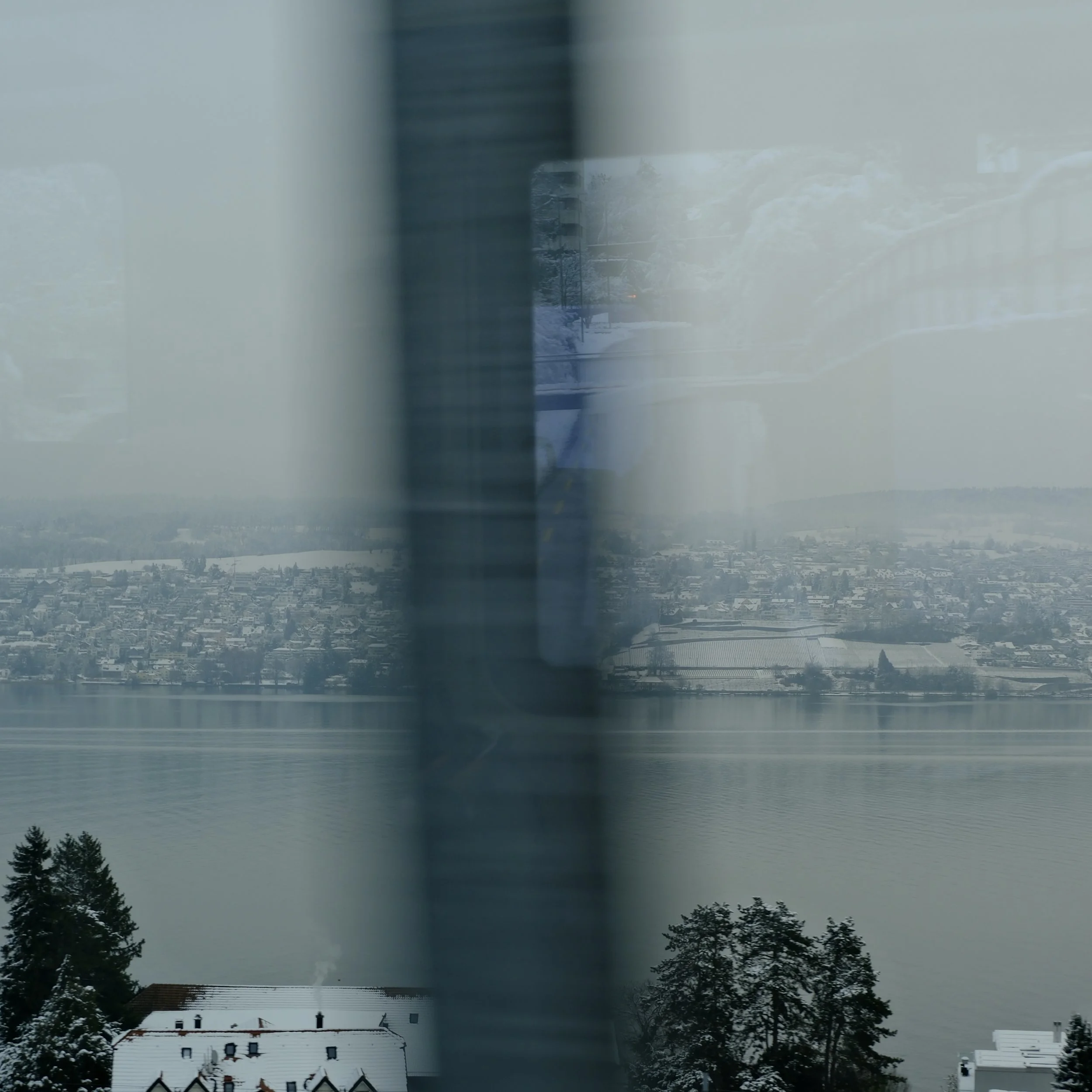 Slippin official single art. Reflection of a train window showing a snowy landscape with houses, trees, and a large body of water.
