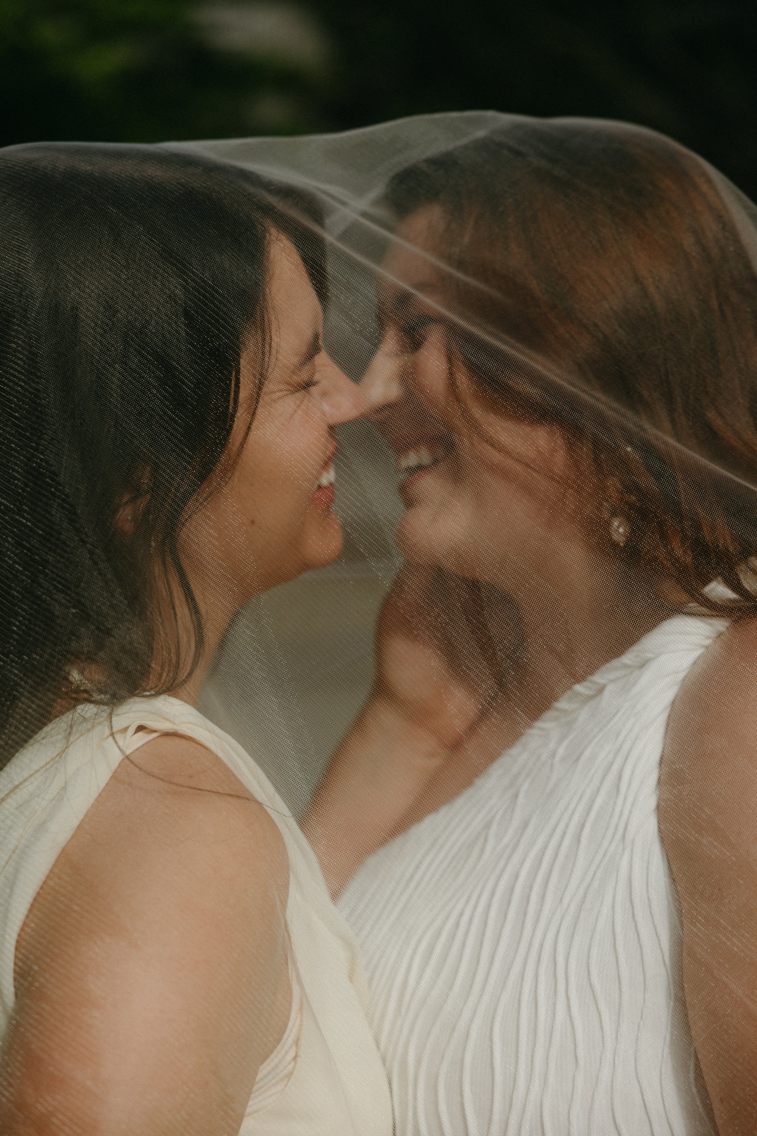 LGBTQ+ brides leaning in for a kiss under a veil in an artistic wedding photo, showcasing same sex wedding planning, lesbian wedding coordination, and professional support for LGBTQ+ couples.
