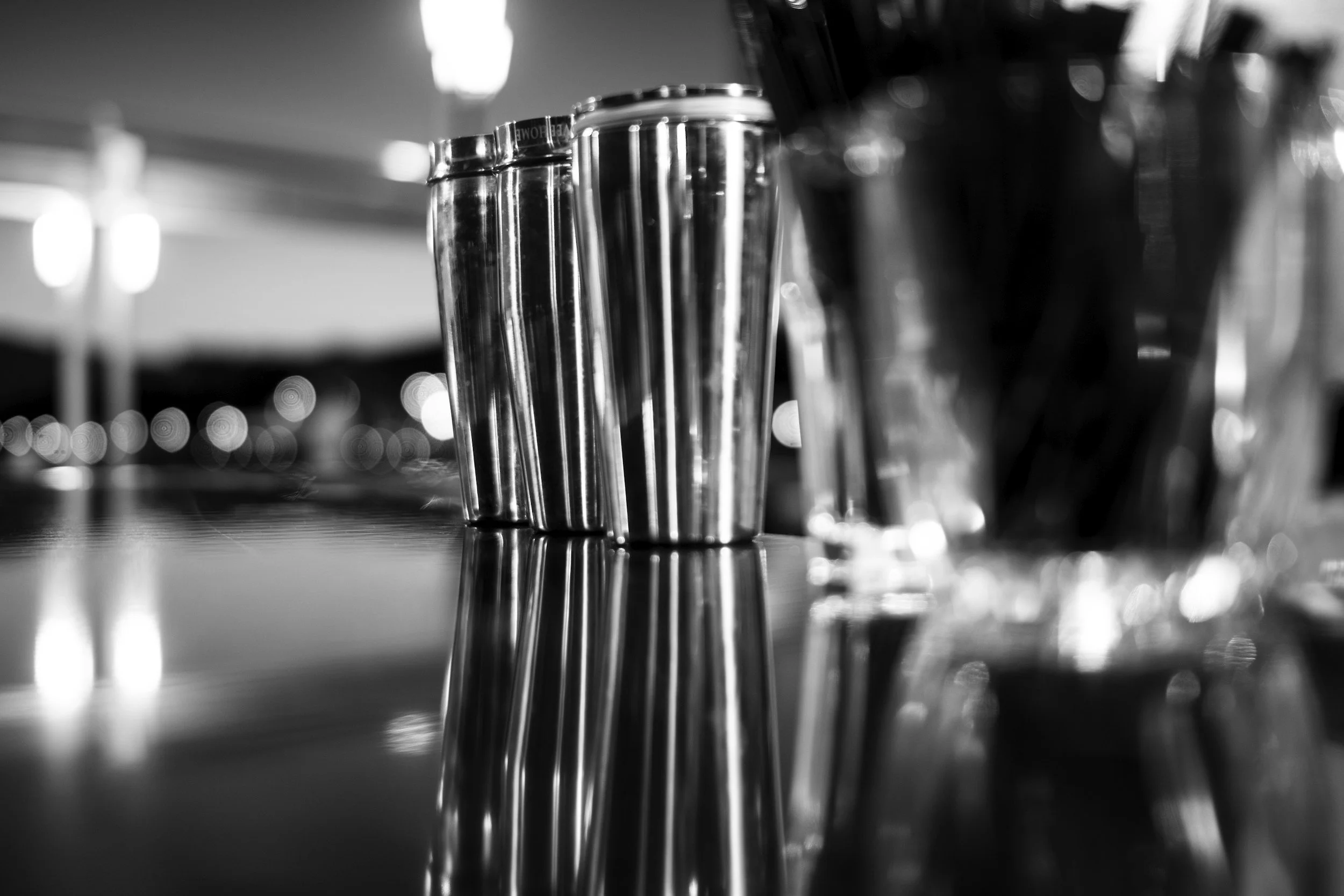 Close-up of stainless steel salt and pepper shakers on a bar or dining table, with blurred lights in the background.