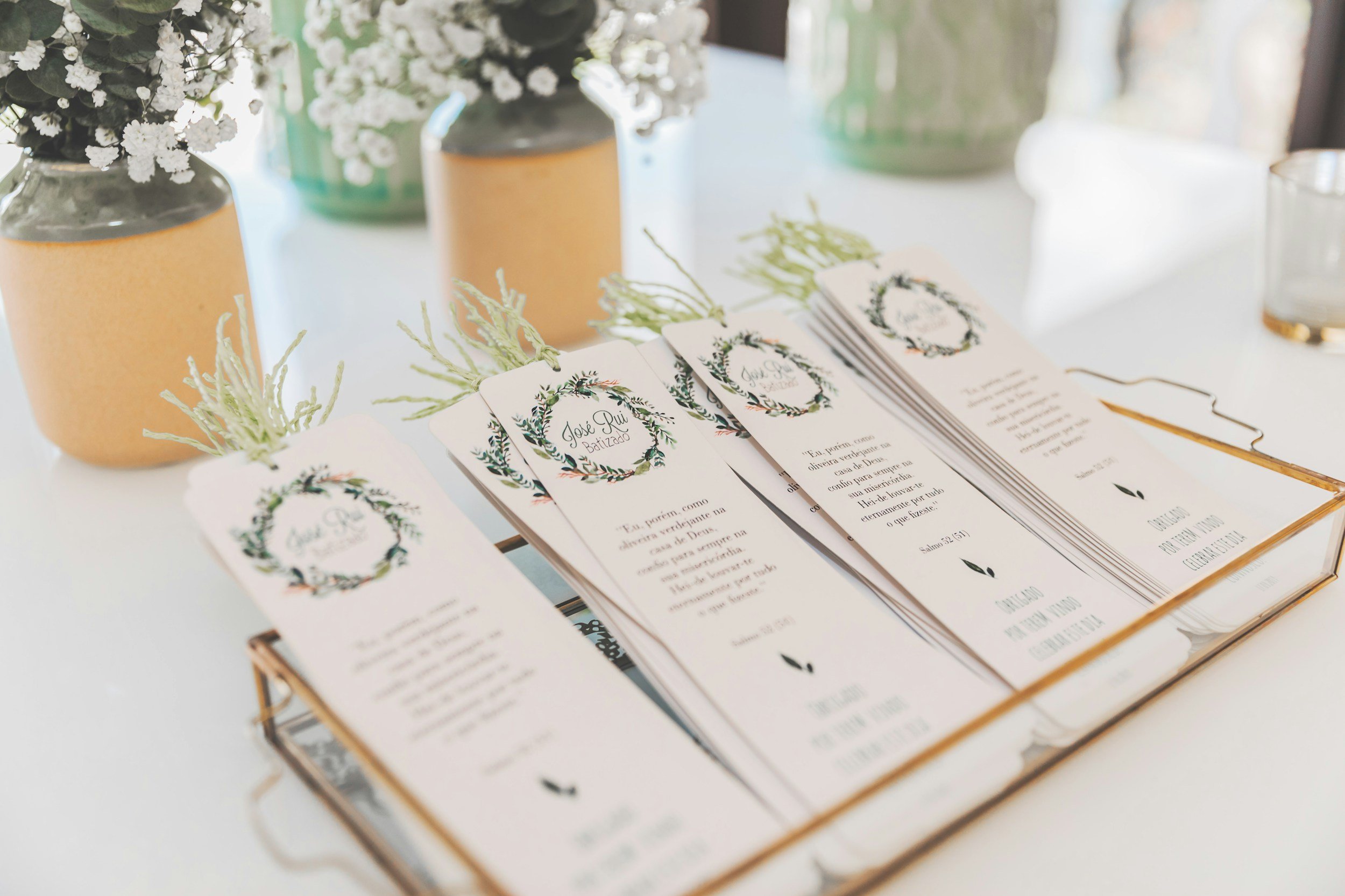 Open book with printed text and wedding program cards decorated with holiday wreath design, along with vases containing white flowers on a table.
