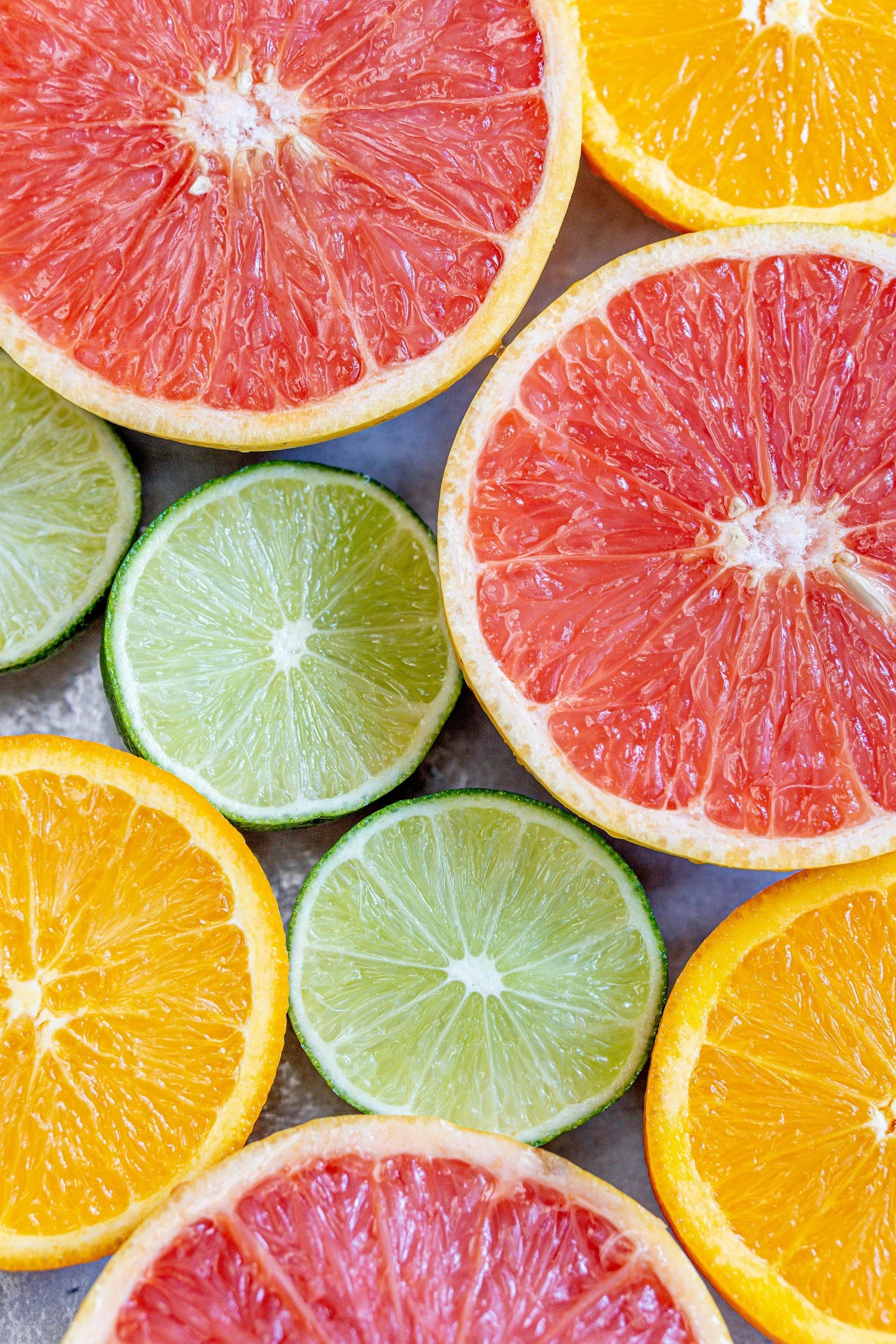 Close-up of sliced citrus fruits, including grapefruit, orange, lemon, and lime, arranged on a flat surface.