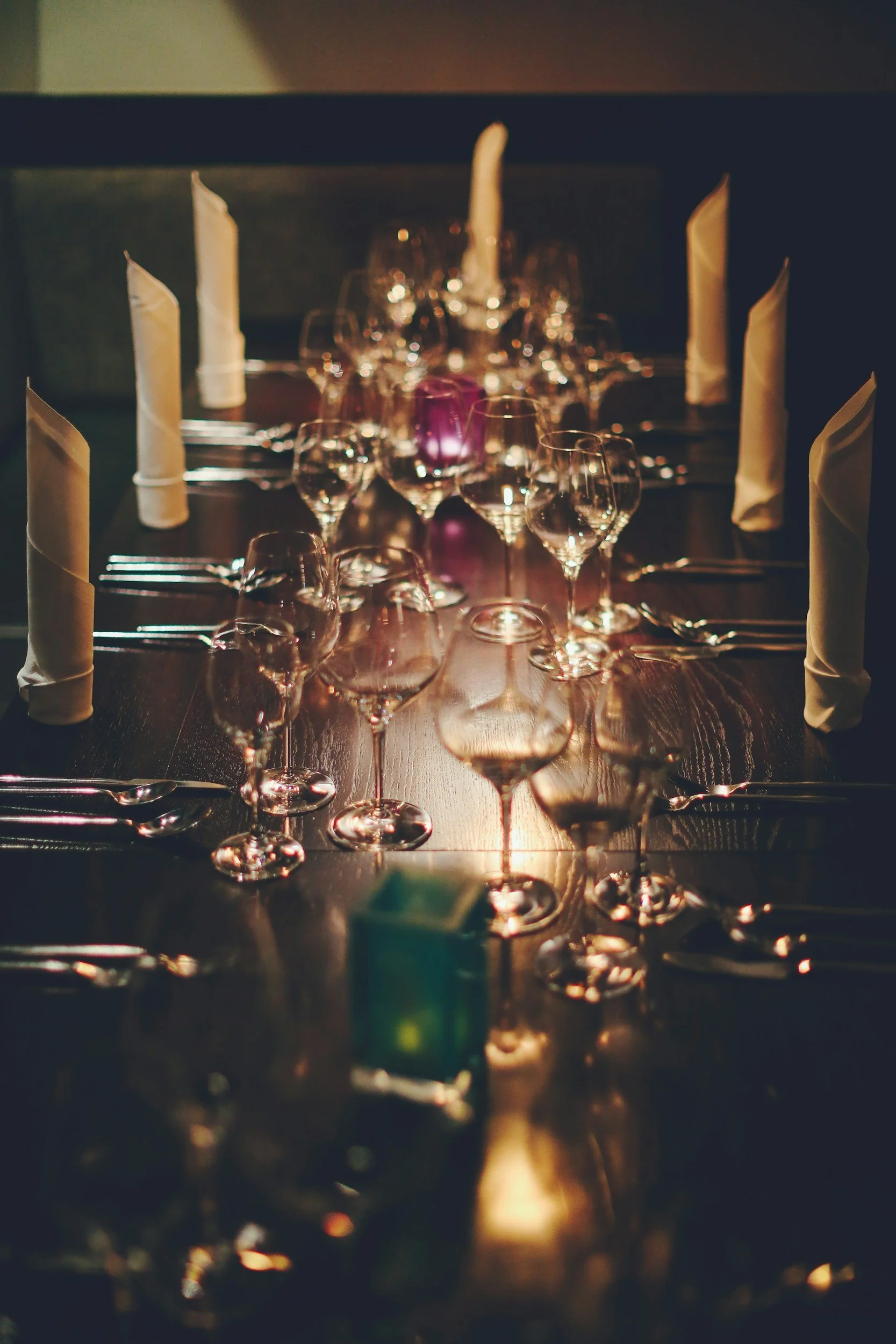 A long dining table set for a formal dinner with multiple wine glasses, candles, and neatly folded napkins.
