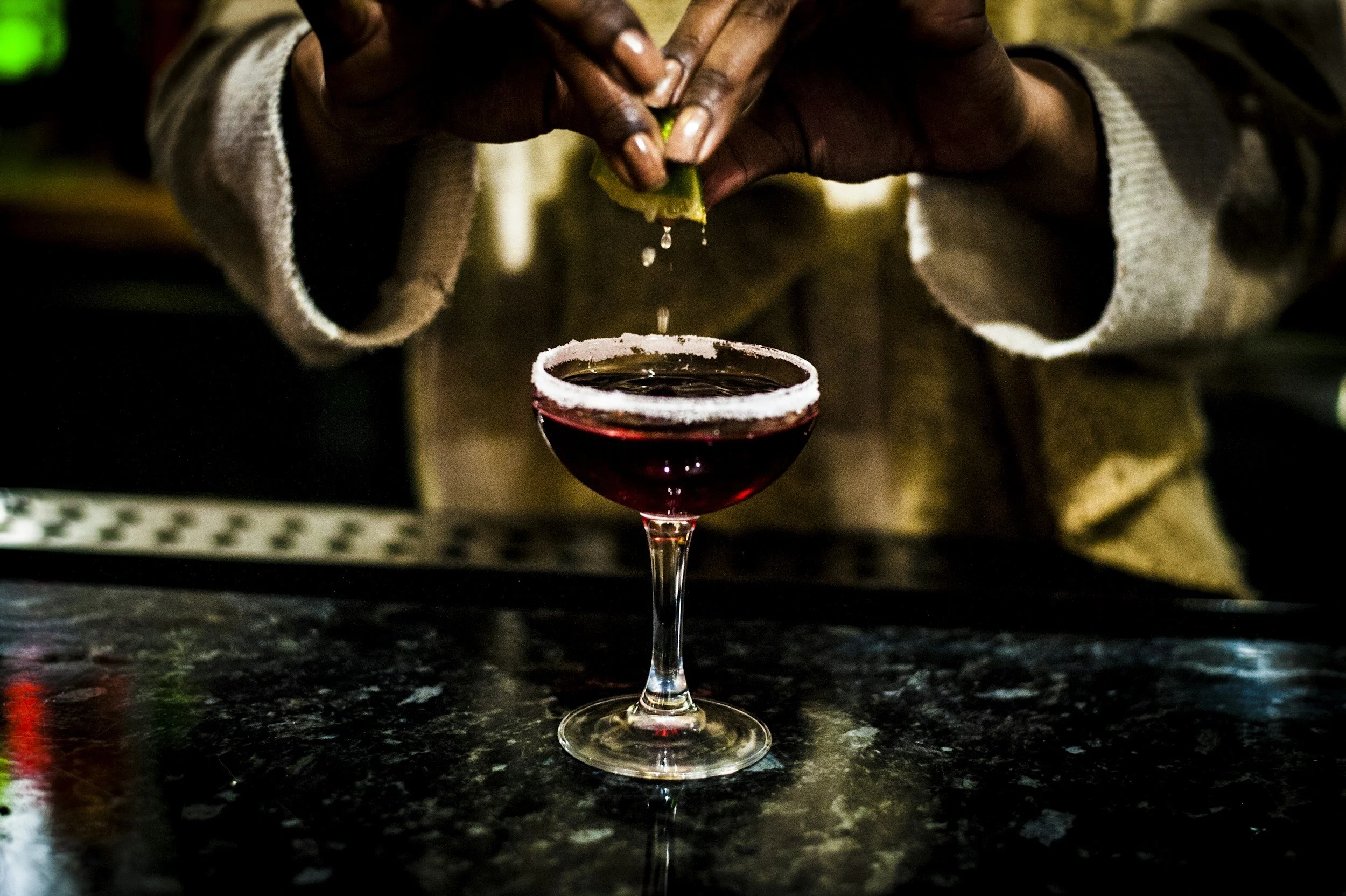 A person squeezing a lime into a glass of red wine on a dark countertop.