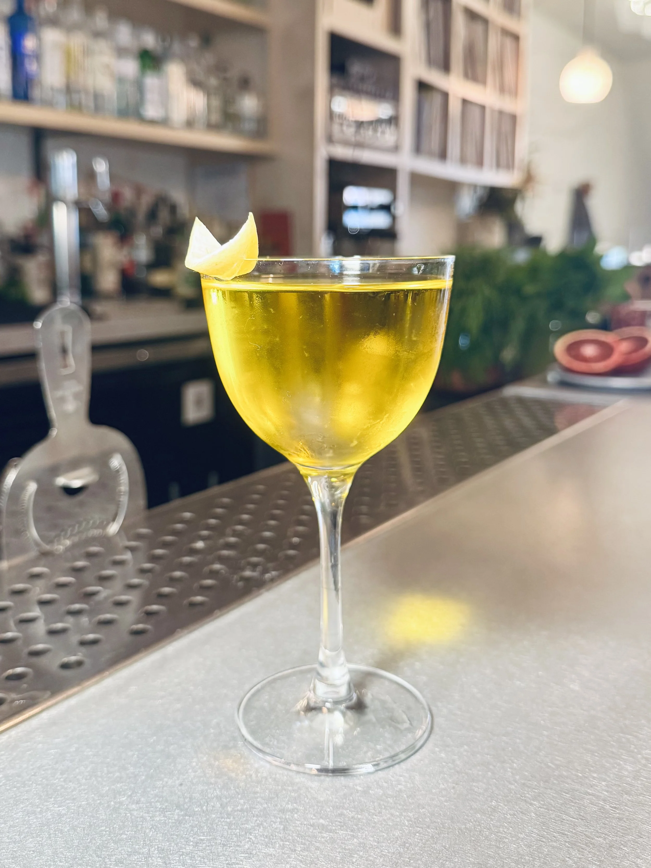 A glass of lemon cocktail with a lemon wedge garnish on the rim, placed on a bar counter.