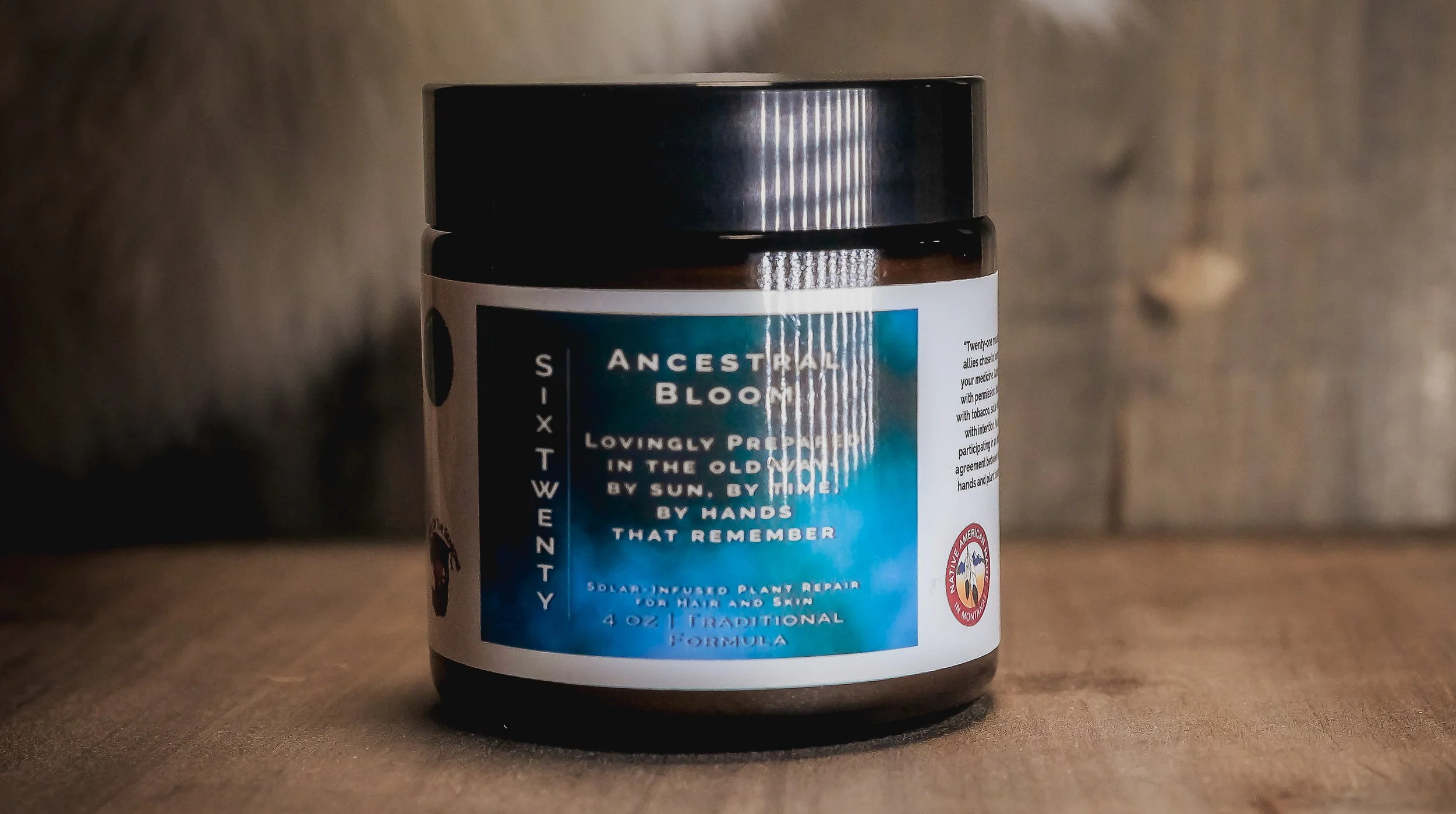 Amber glass jar of Ancestral Bloom plant repair balm, featuring a deep blue label with poetic messaging, placed on a wooden surface with fur background.