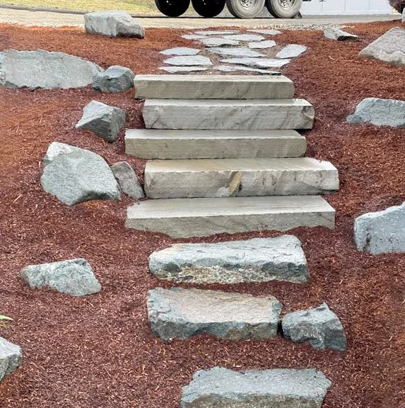 Concrete steps leading up a small hill, surrounded by red mulch and large rocks.