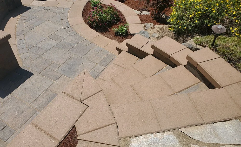 Curved walkway made of brick and stone pavers leading up to garden with plants and flowers, with landscape lighting along the path.