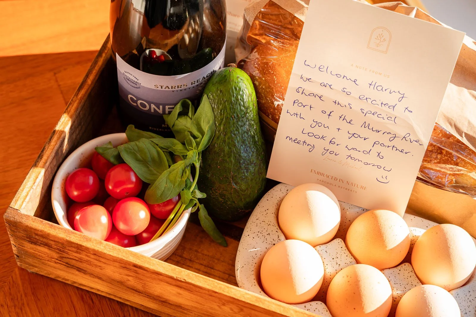A selection of items in a tray, eggs, cherry tomato, avocado, wine, welcome note for guests arriving to the accommodation