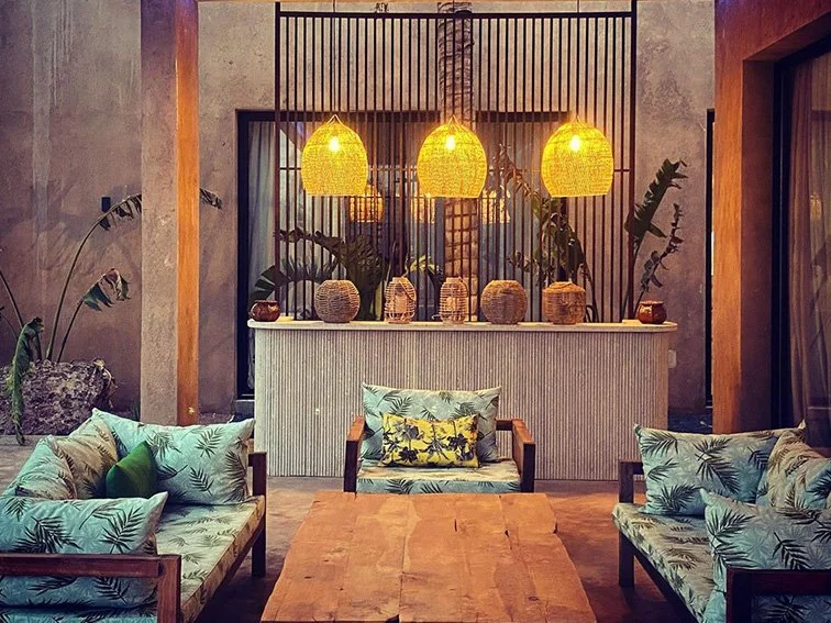 Tropical-themed outdoor seating area with wicker lamps, wooden furniture, and plant-patterned cushions.