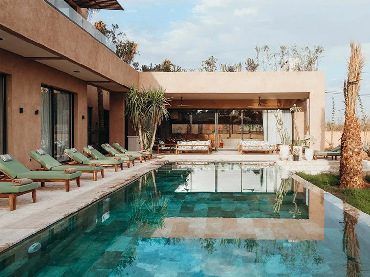 Modern luxury villa with a swimming pool, sun loungers, and patio seating area, featuring minimalist architecture and tropical plants.