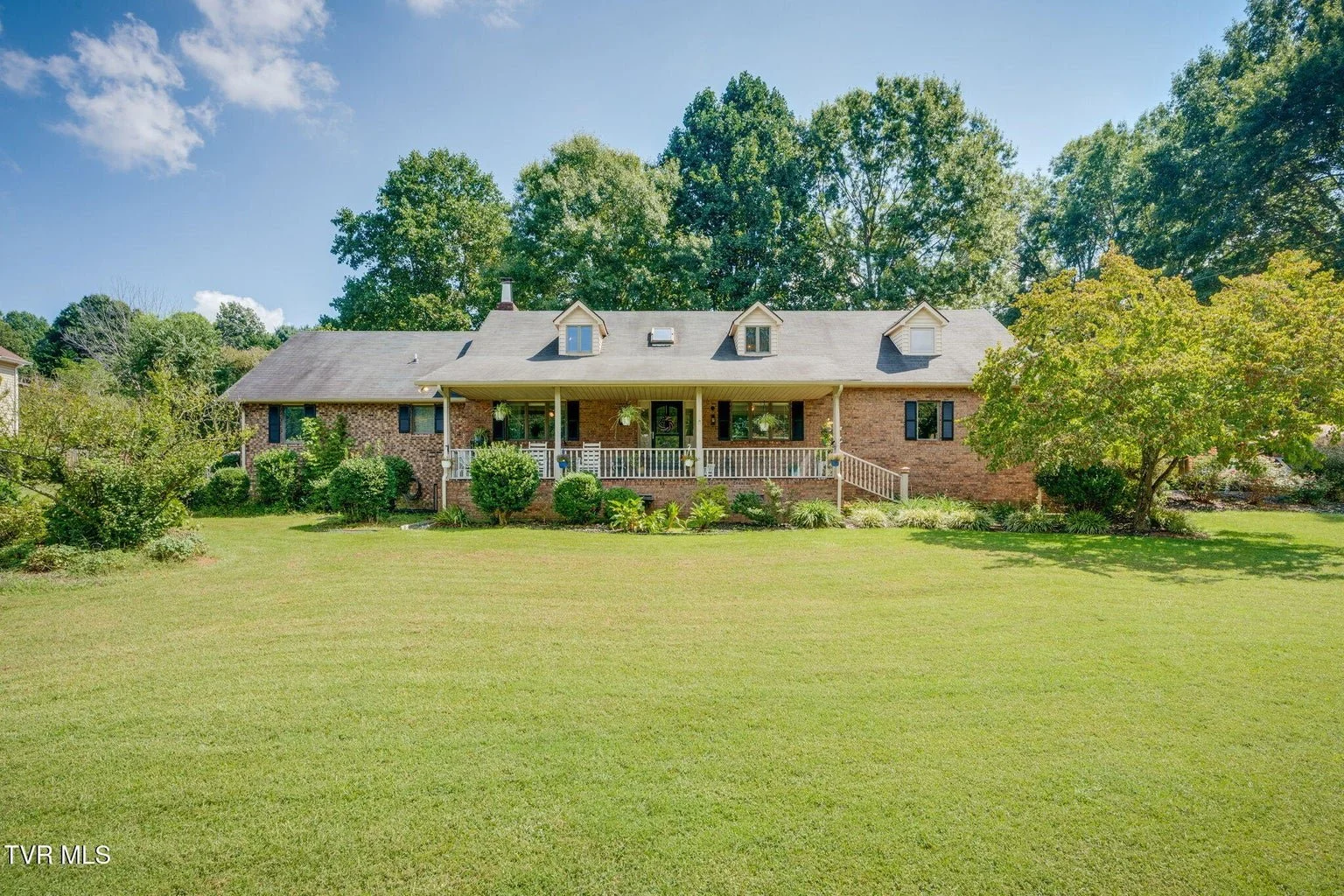 Brick house with a large front yard and a covered porch, surrounded by lush green trees.