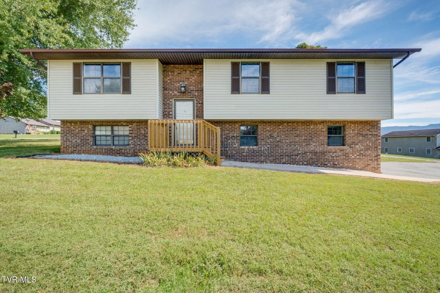Back view of a two-story house with brick foundation and beige siding, small front porch with wooden stairs, green lawn. A real Estate listing in Mount Carmel, Tennessee listed by Sherry Ludecker