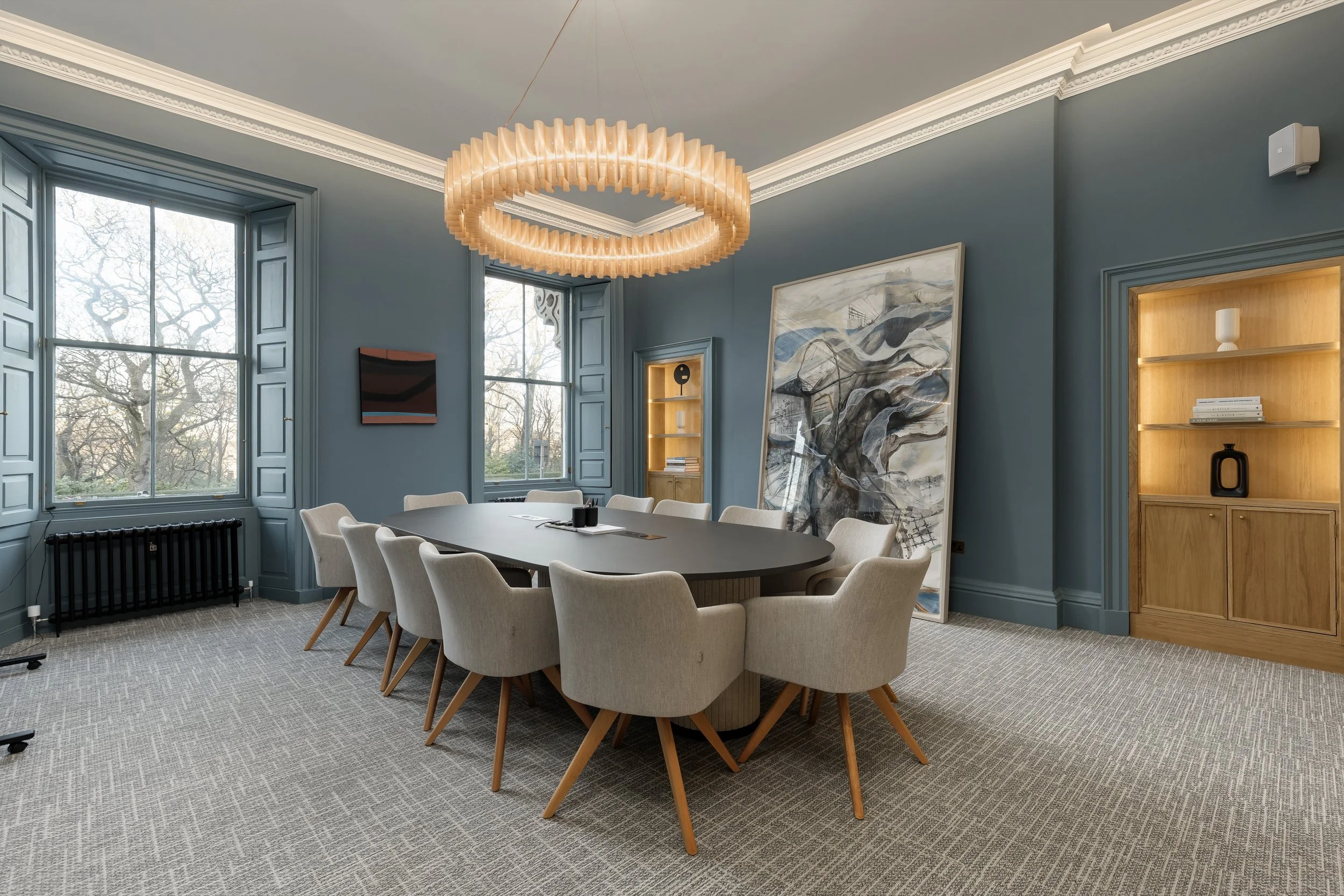 Boardroom space with 12 grey chairs and a blue/grey matte painted room. Room is Goergian and features grand windows at the far end. Painting in middle of the room going from floor to ceiling. Boardroom/meeting Room in New Town Edinburgh for business