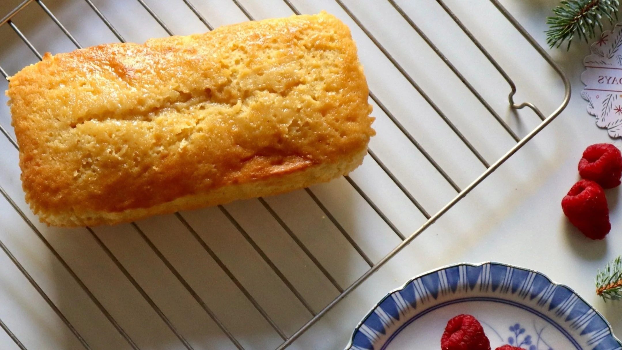 Loaf of cornbread cooling on a wire rack, with decorative plates and raspberries nearby.
