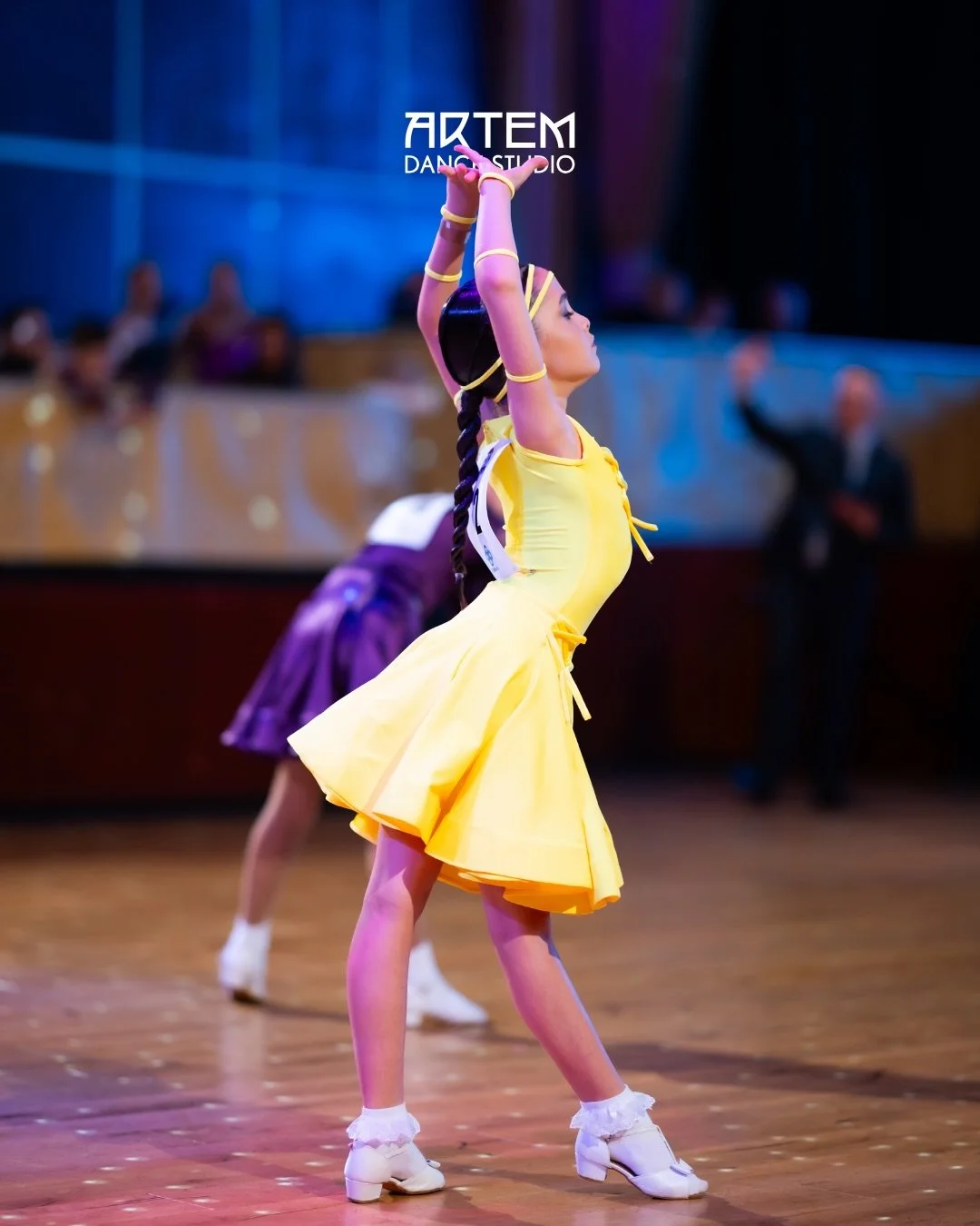 Child dancer in a yellow dress performing on stage at a kids dance competition.