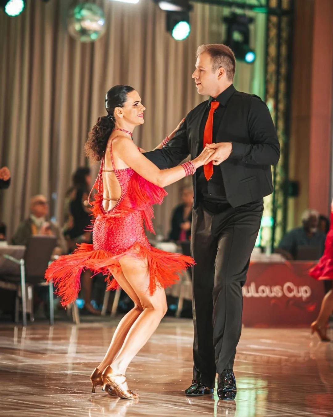 Latin ballroom dance couple performing at a competition, the woman in a pink fringe dress with dynamic movement on the dance floor