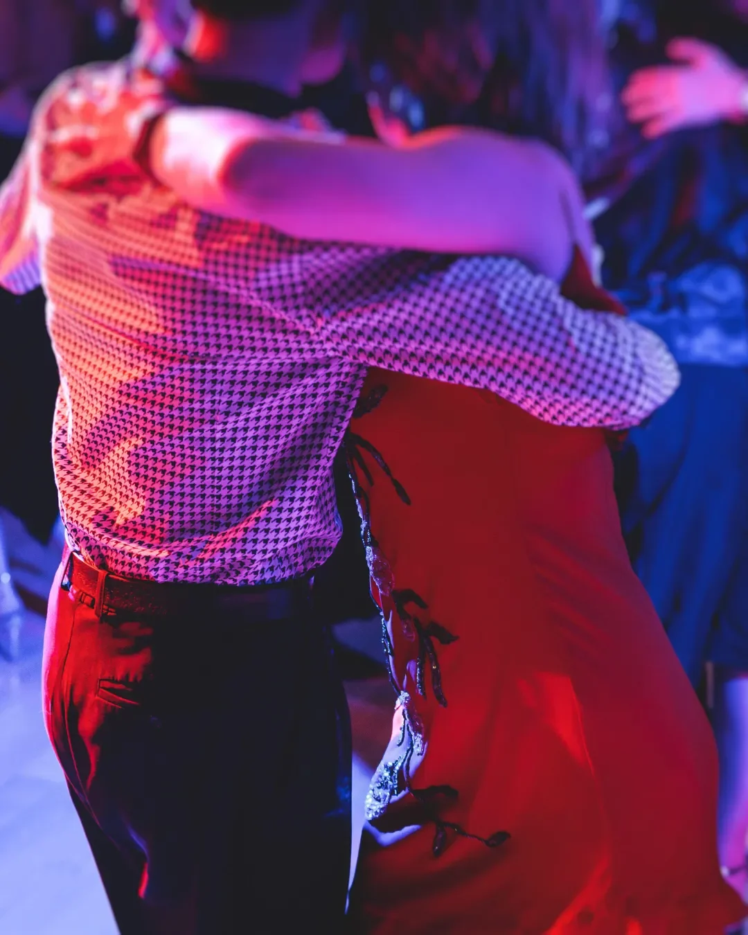 Close-up of a couple dancing at a social dance event under atmospheric red and blue lighting
