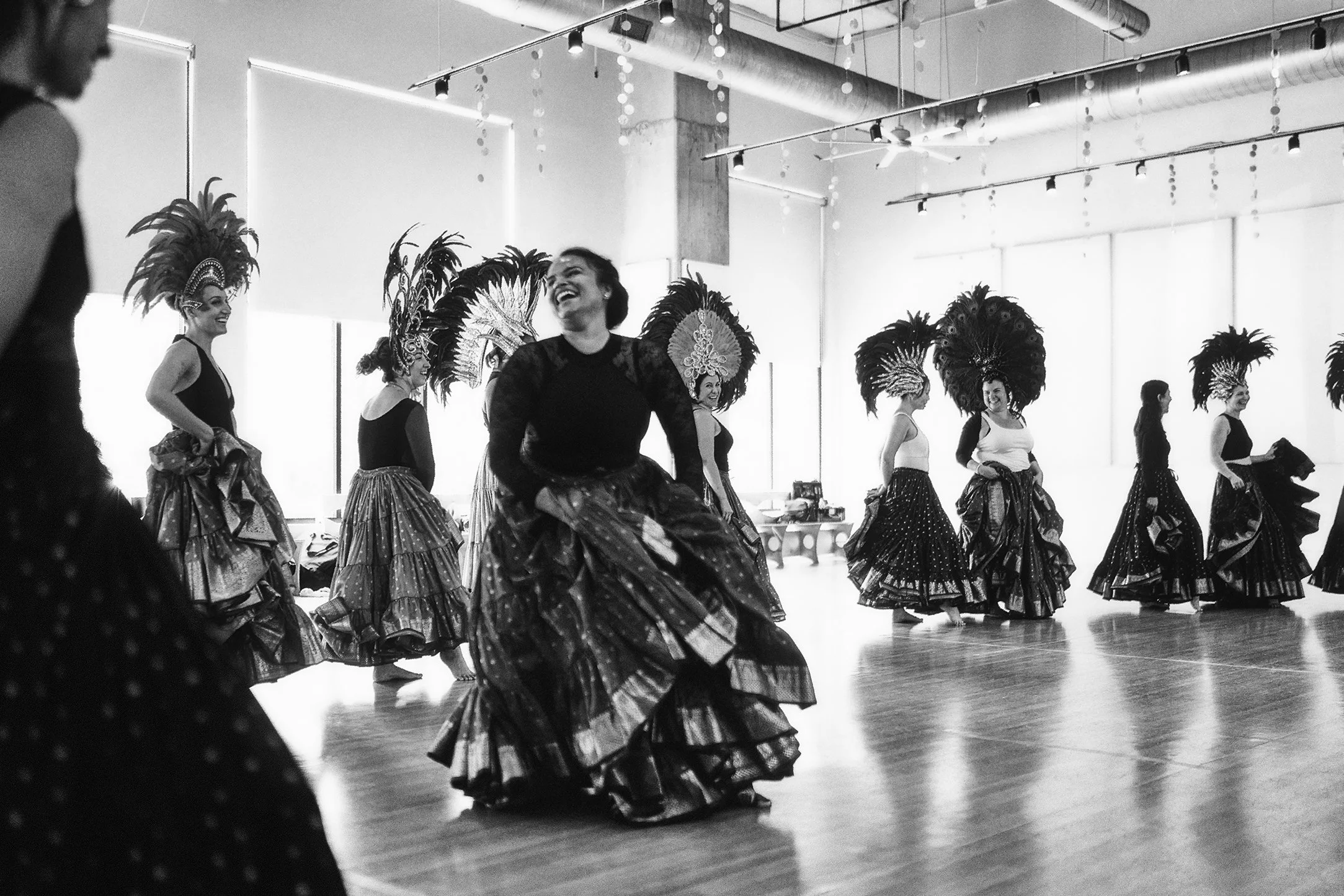 Women in elaborate costumes with feathered headdresses practicing traditional dance in a dance studio.