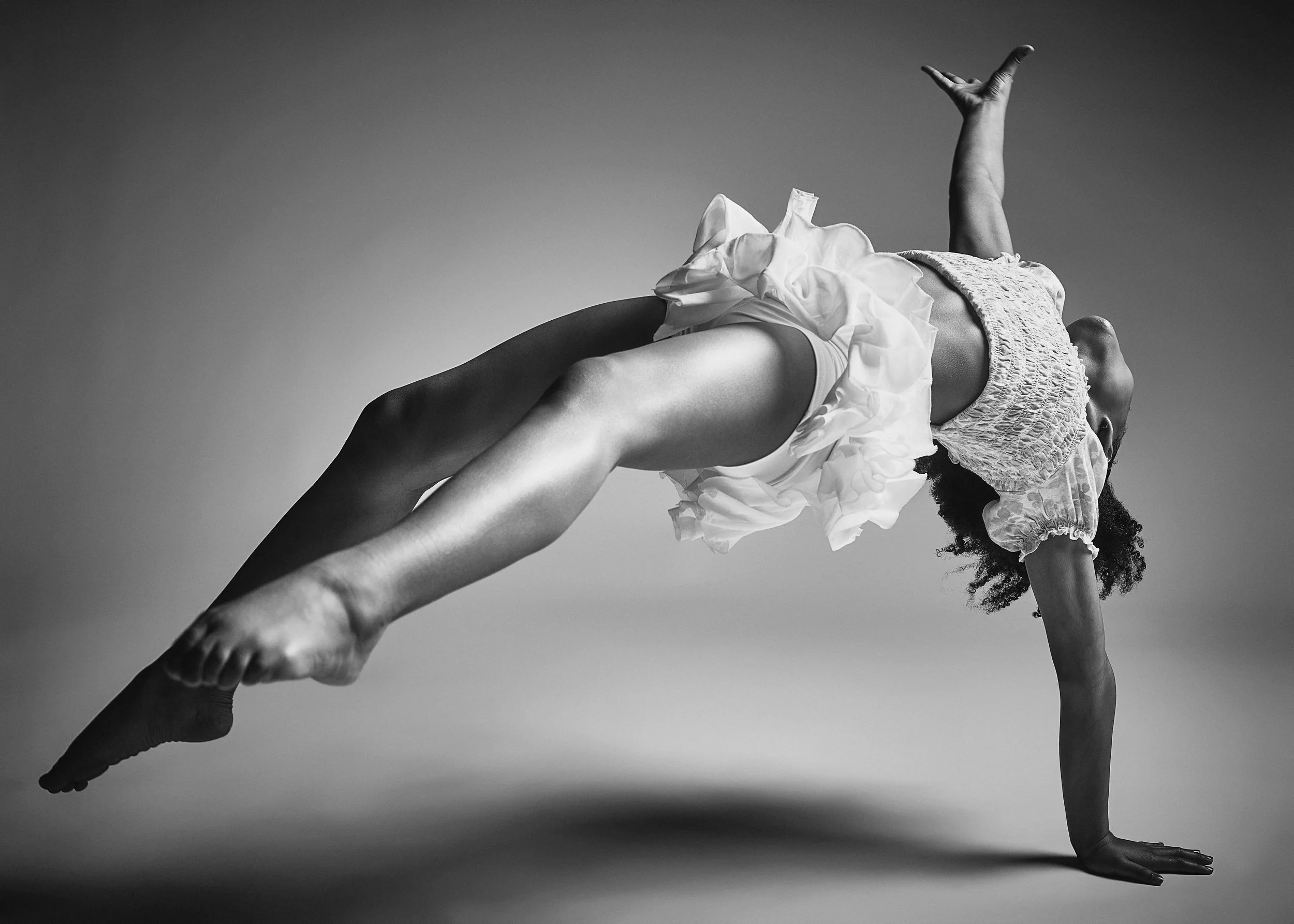 A woman performing a handstand in a studio, wearing a lace top and a ruffled skirt, captured in black and white.