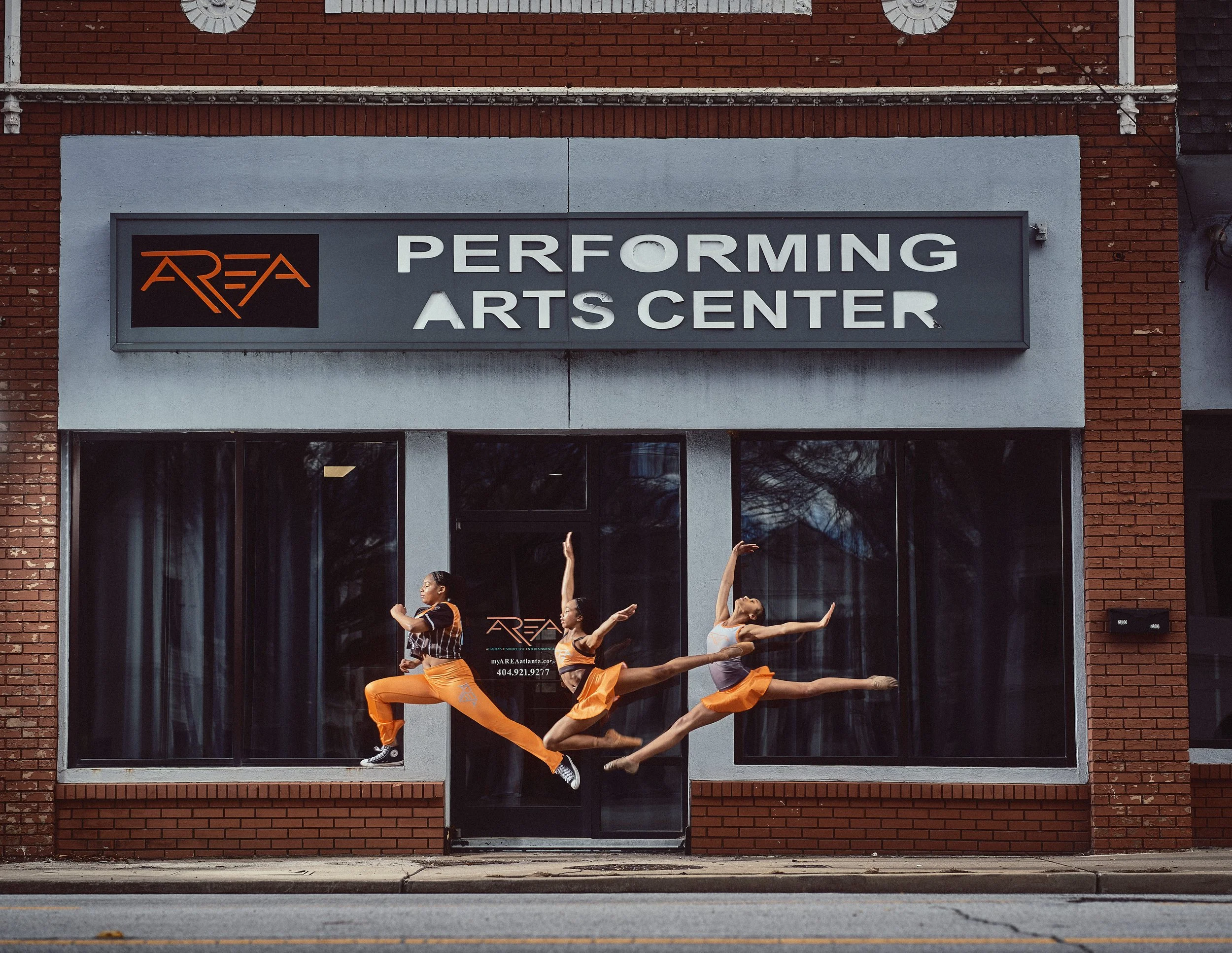 Three dancers jumping in front of a performing arts center building.