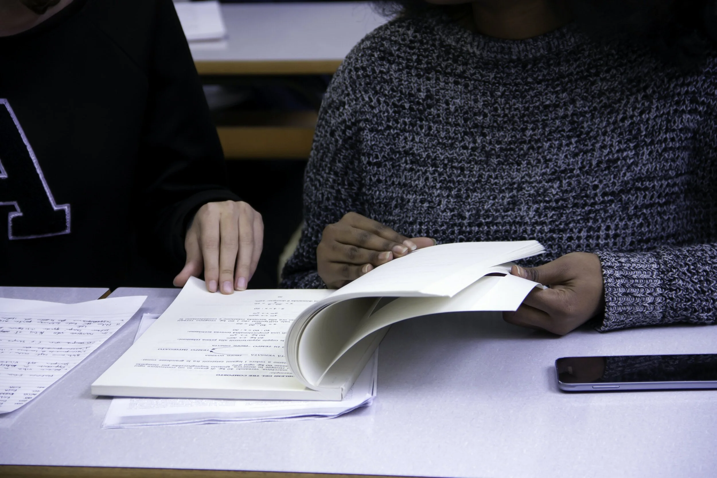Two people looking at an open book and some papers on a table