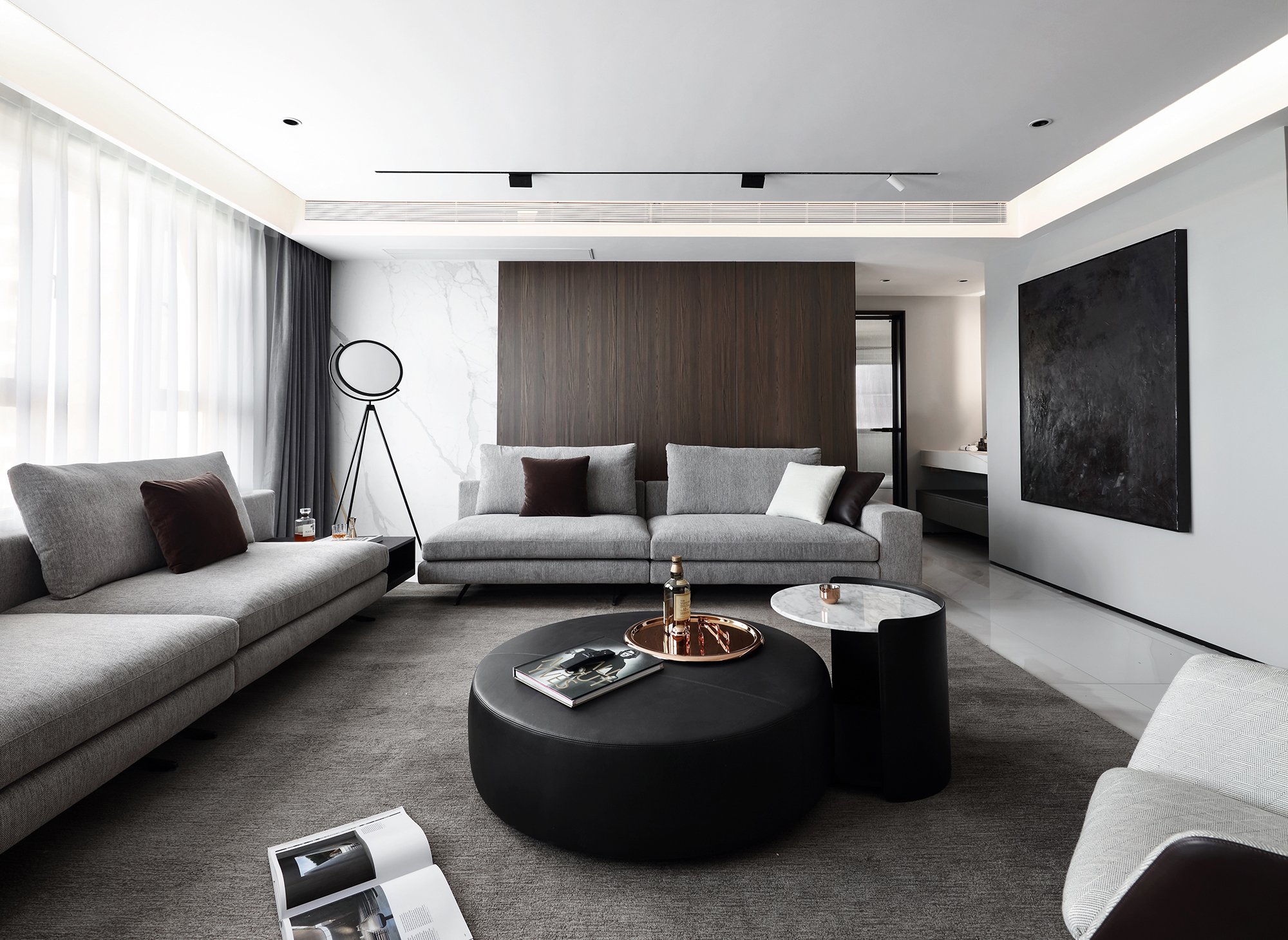 Modern living room with gray sofas, round ottoman, side table, floor lamp, large abstract painting, and neutral decor.