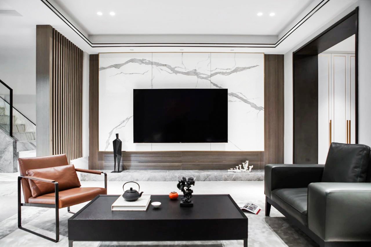 Modern living room interior with marble accents, black TV mounted on wall, brown leather chair, black sofa, tea set on coffee table, and decorative sculpture.