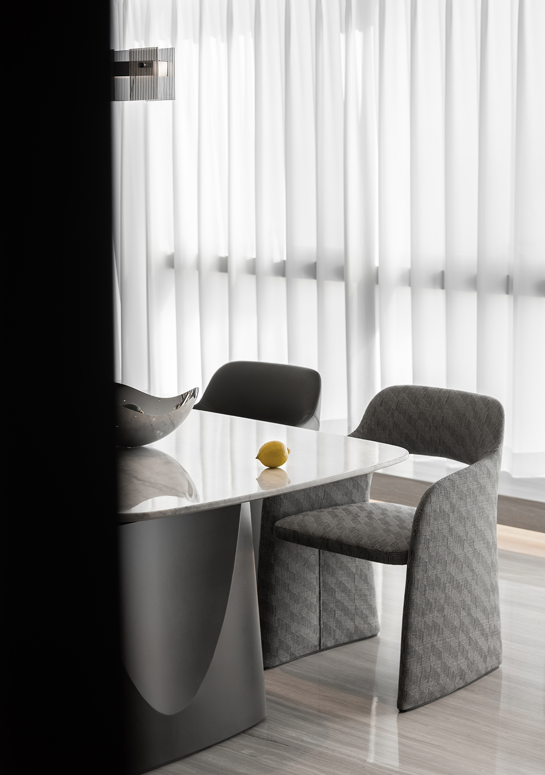 Modern dining room with a marble table, a lemon, gray-patterned chairs, and white curtains.