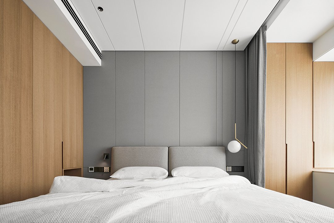 Modern minimalist bedroom with gray upholstered headboard, wooden wall panels, white bedding, and a hanging spherical light fixture.