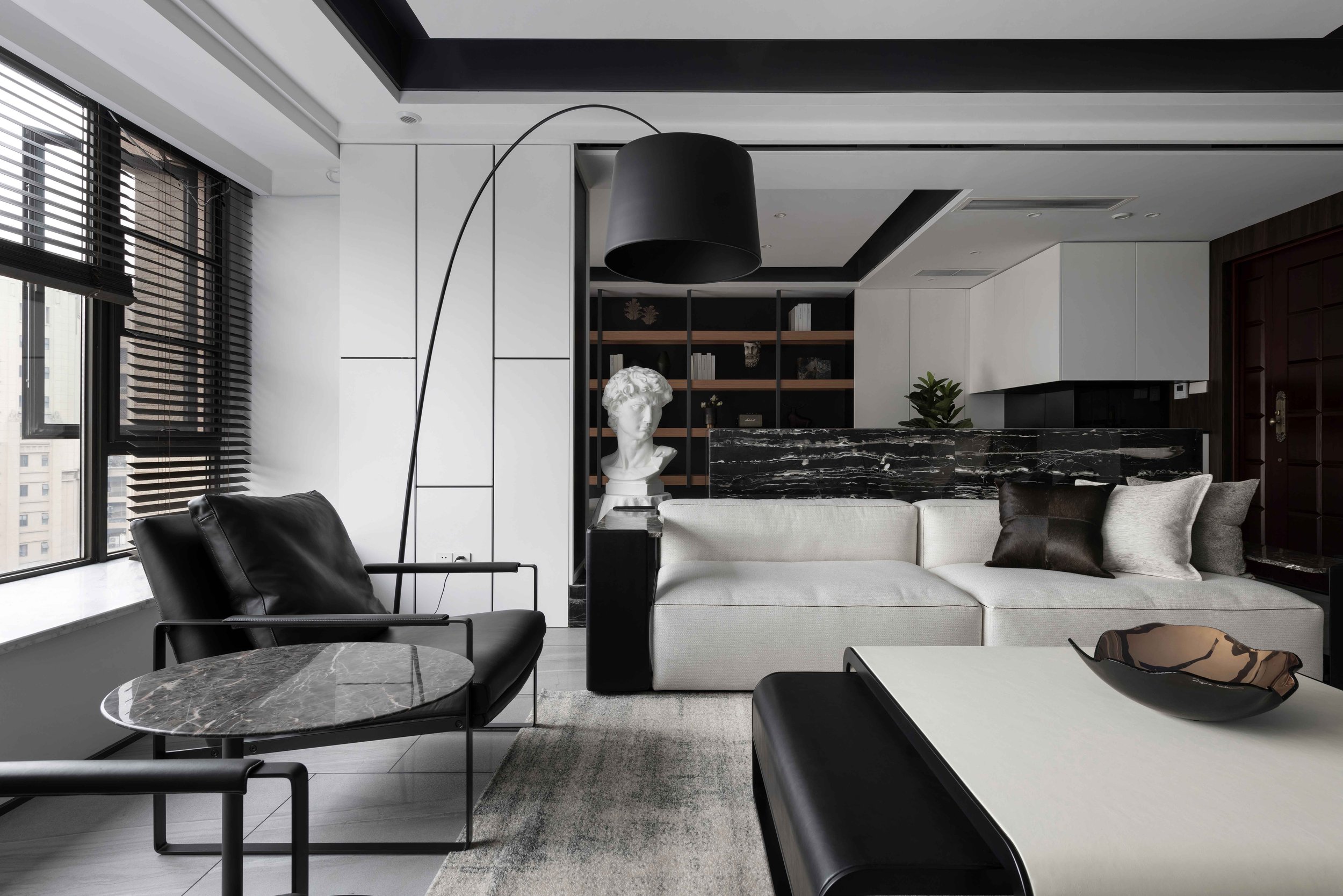 Modern living room interior with black and white furniture, marble table, floor lamp, and decorative bust.