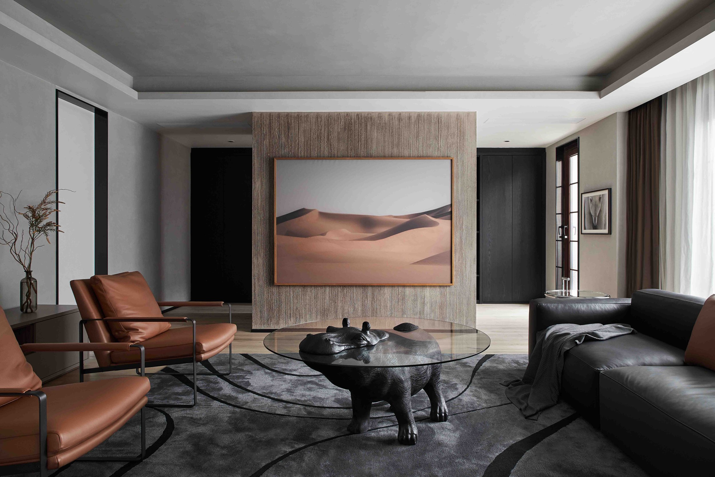 Modern living room with leather chairs, hippo-shaped glass coffee table, large desert landscape artwork, and dark gray couch.
