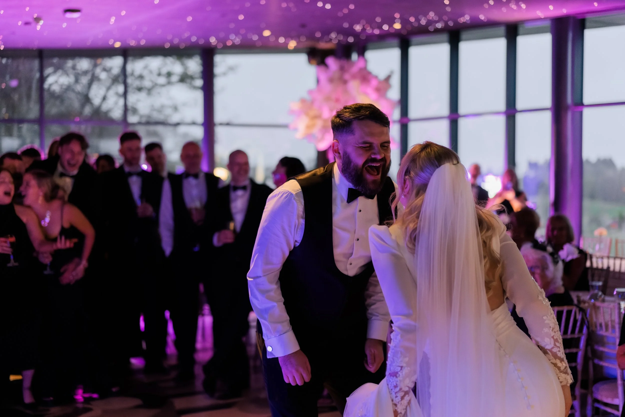 Groom and bride dancing at wedding reception with guests in background