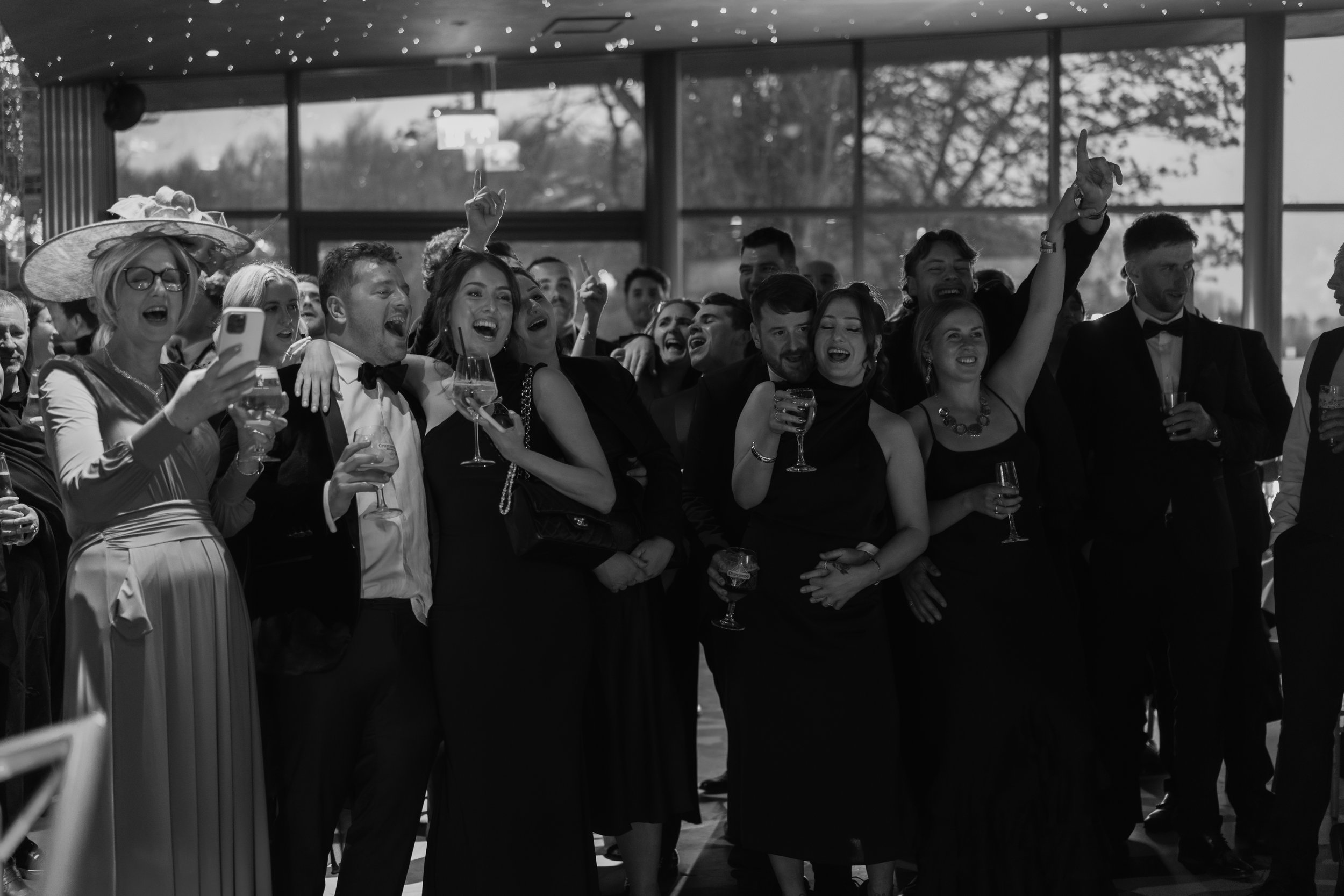 Group of people at a celebration or party, dressed in formal attire, holding drinks, smiling, and enjoying themselves.