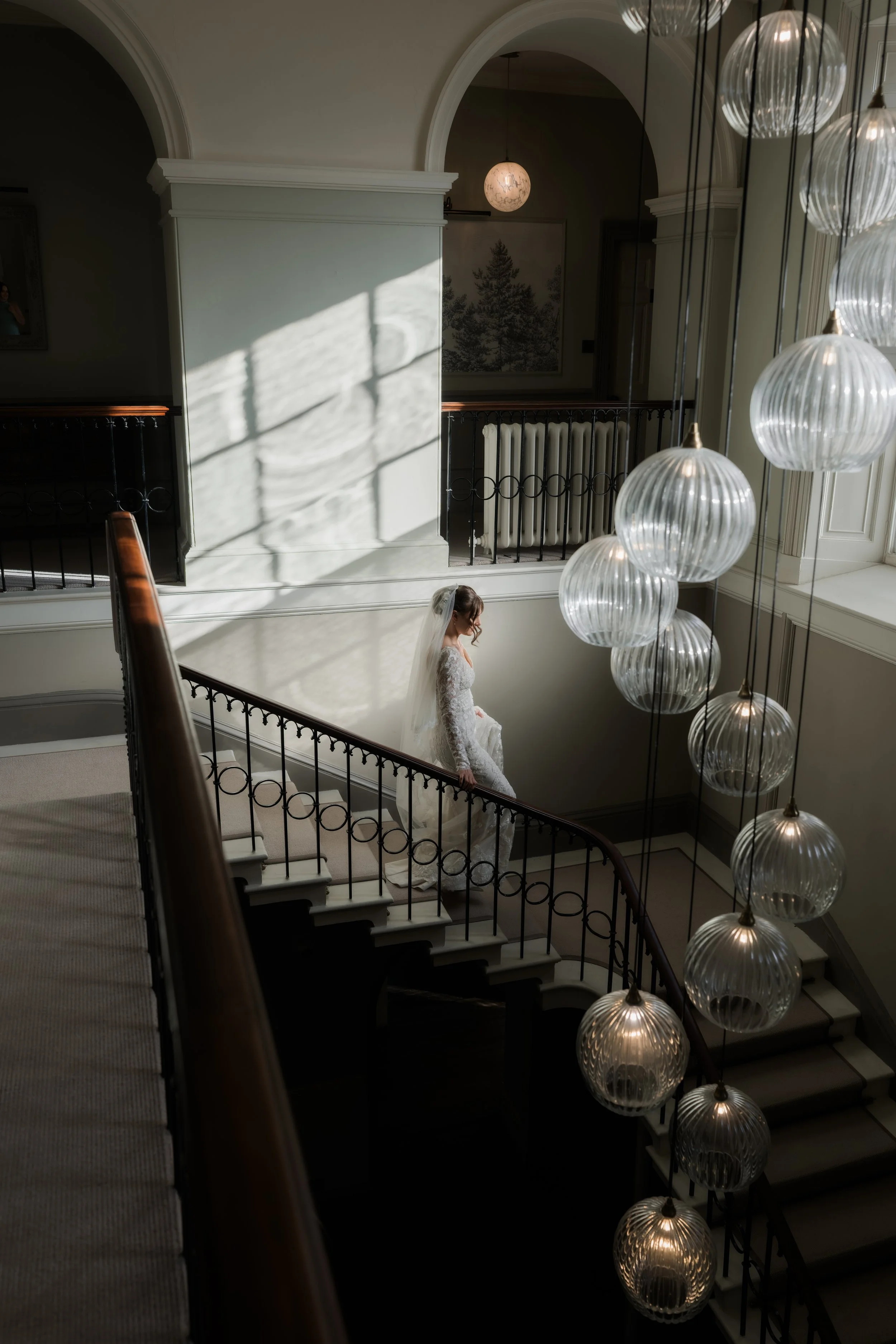 Bride walks down grand staircase through shaft of light at Saltmarshe Hall
