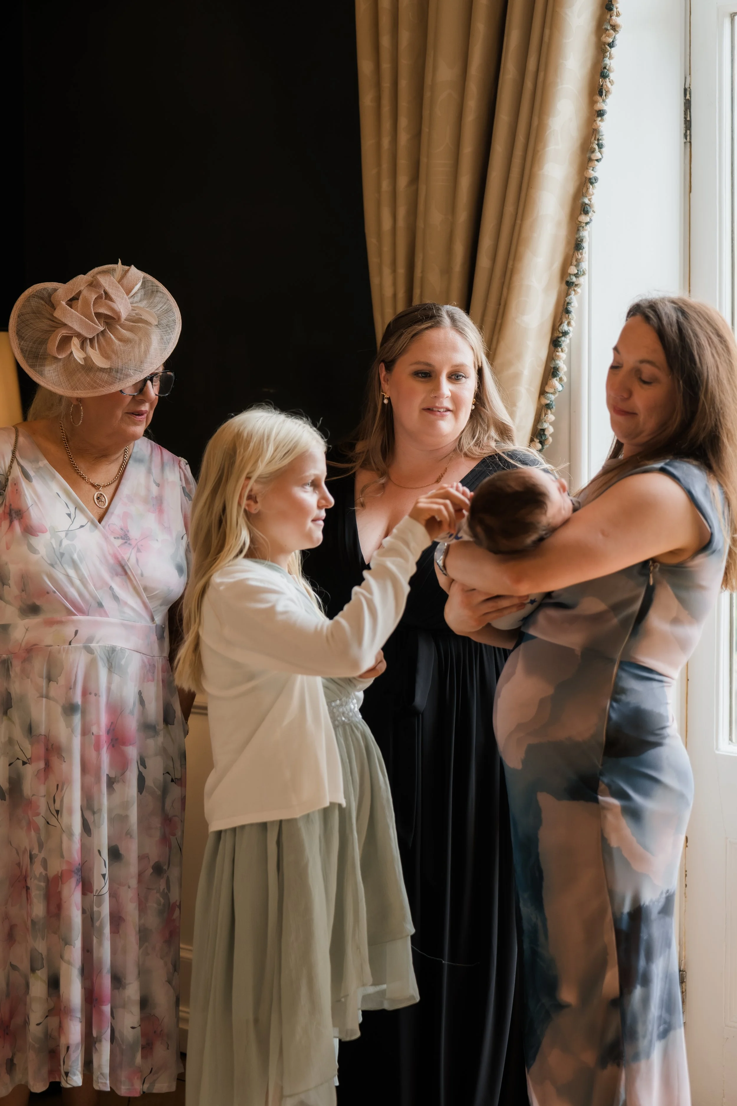 Group of five women gathered near a window, one holding a newborn baby and another touching the baby's hand.