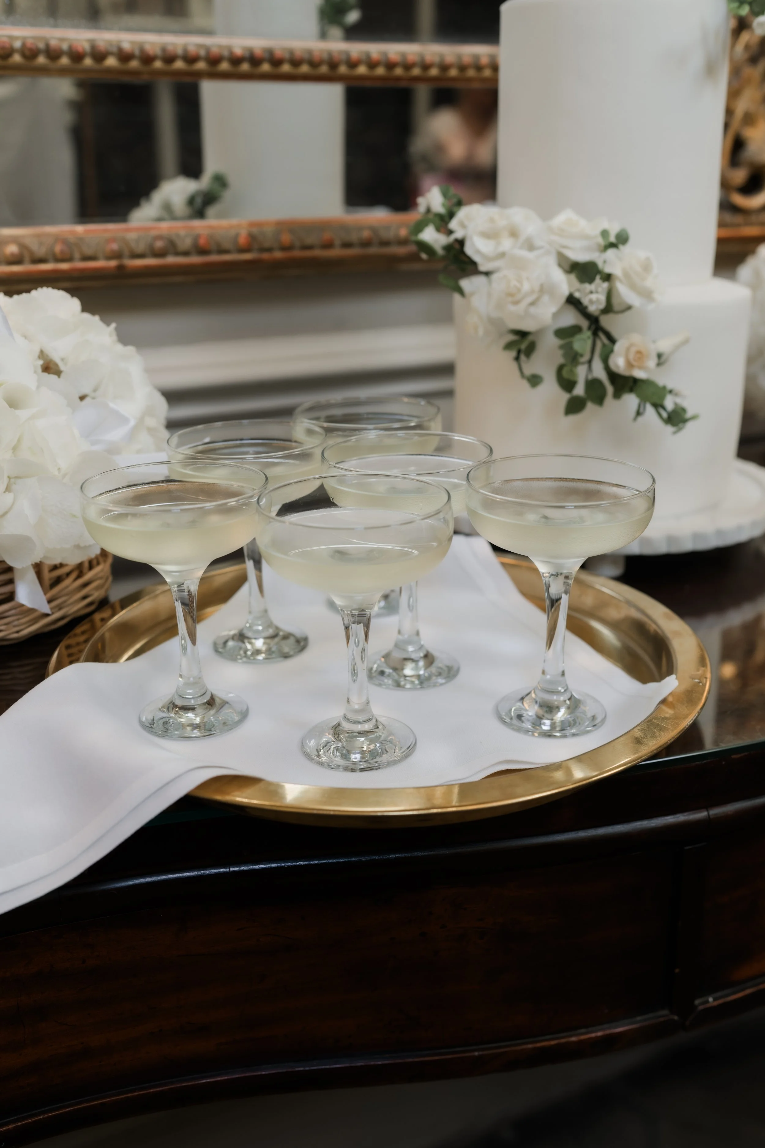 Tray with champagne flutes filled with sparkling wine, decorated with white flowers and greenery, set on a table with a white cloth.