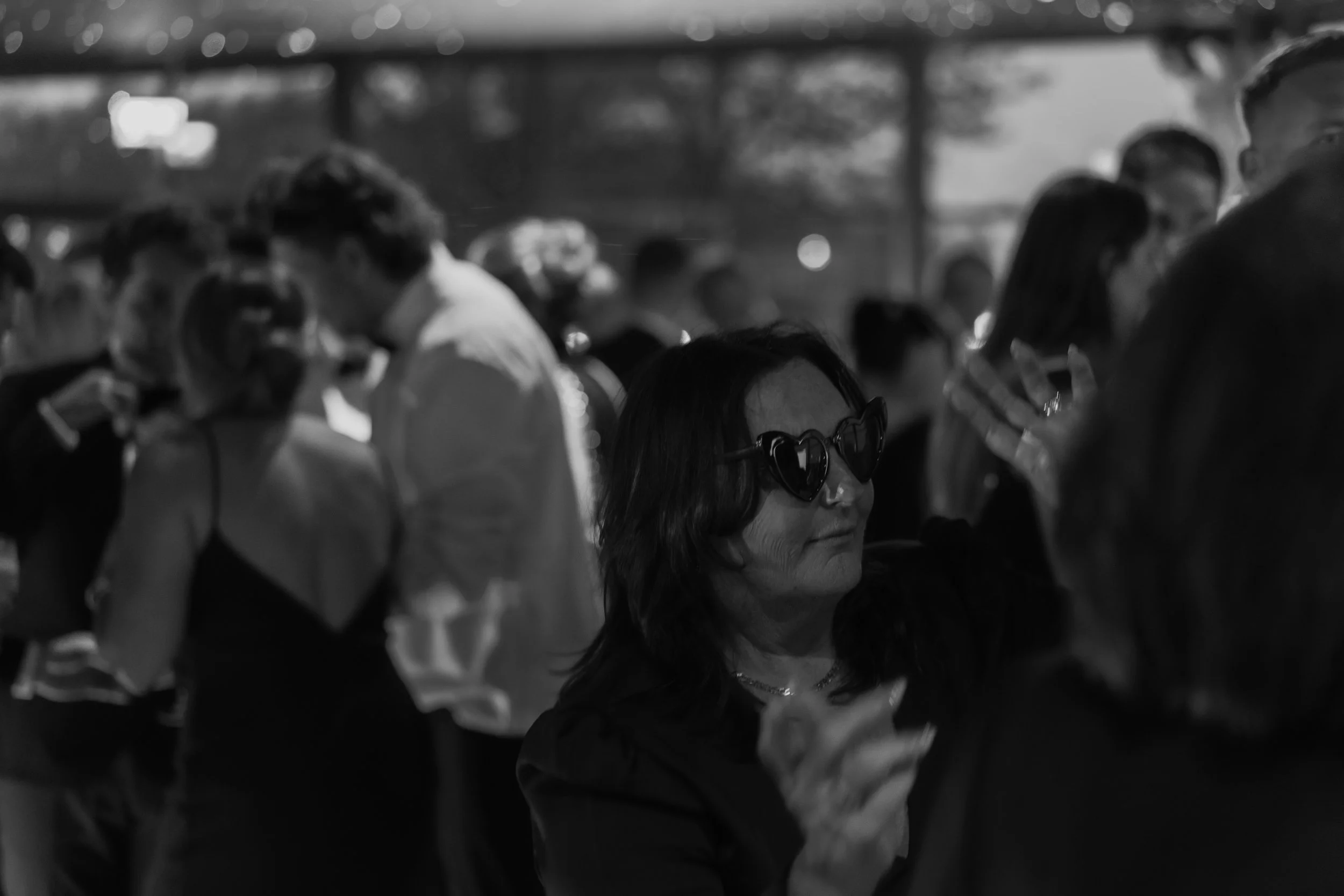 A woman wearing heart-shaped sunglasses dancing at a crowded event in black and white.