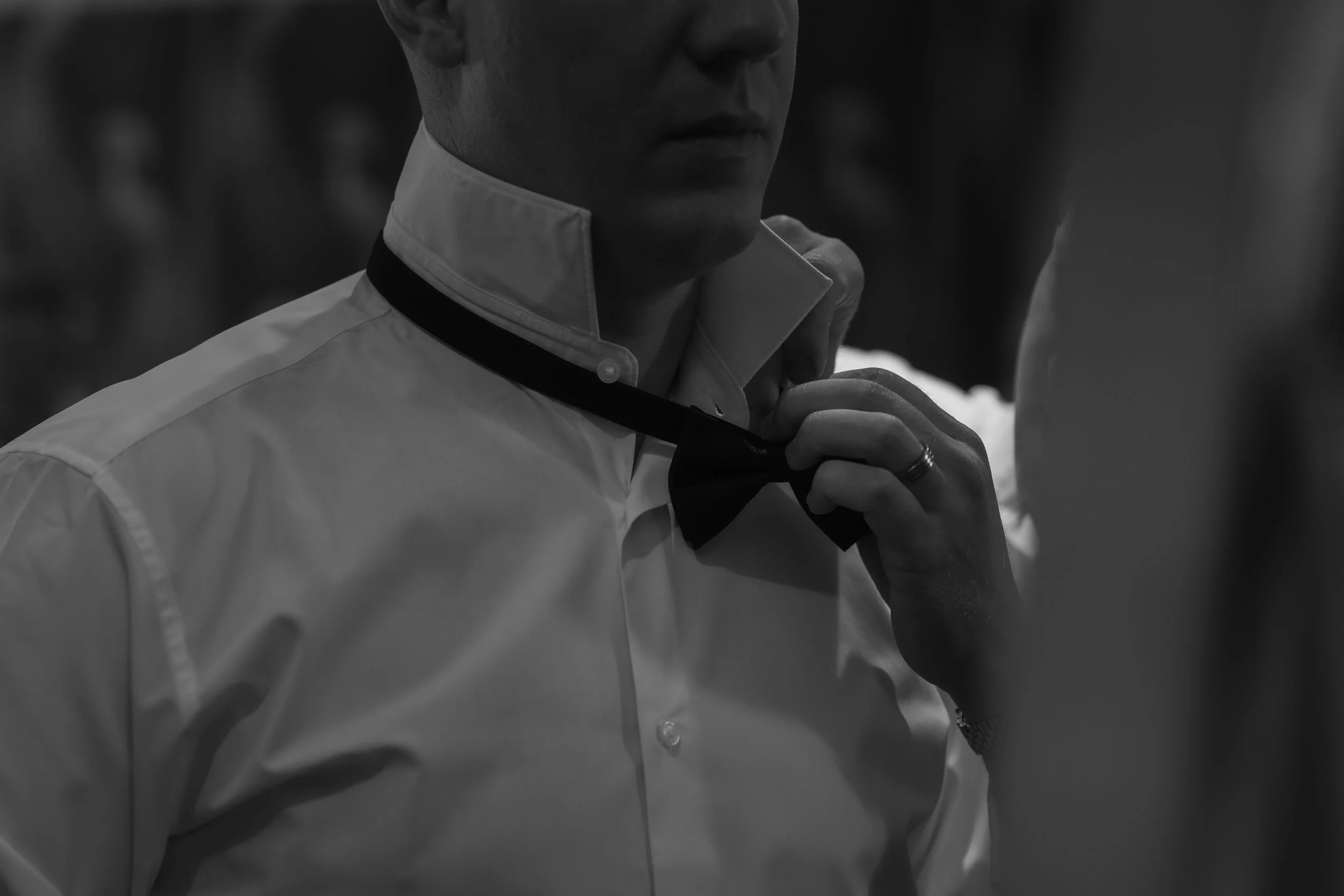 Man adjusting a black bow tie in black and white image.
