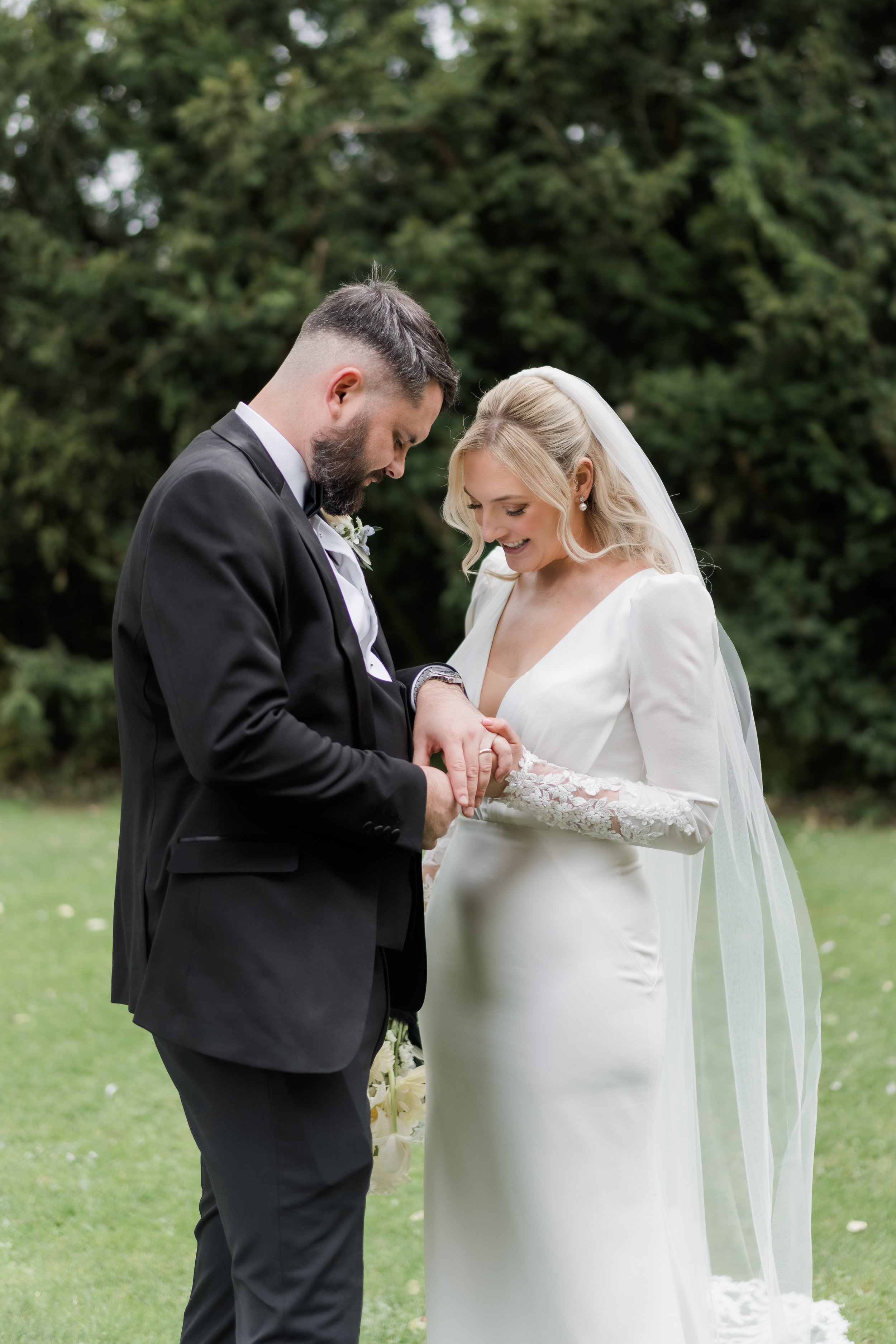 A bride and groom holding hands during their wedding ceremony outdoors, with trees in the background.