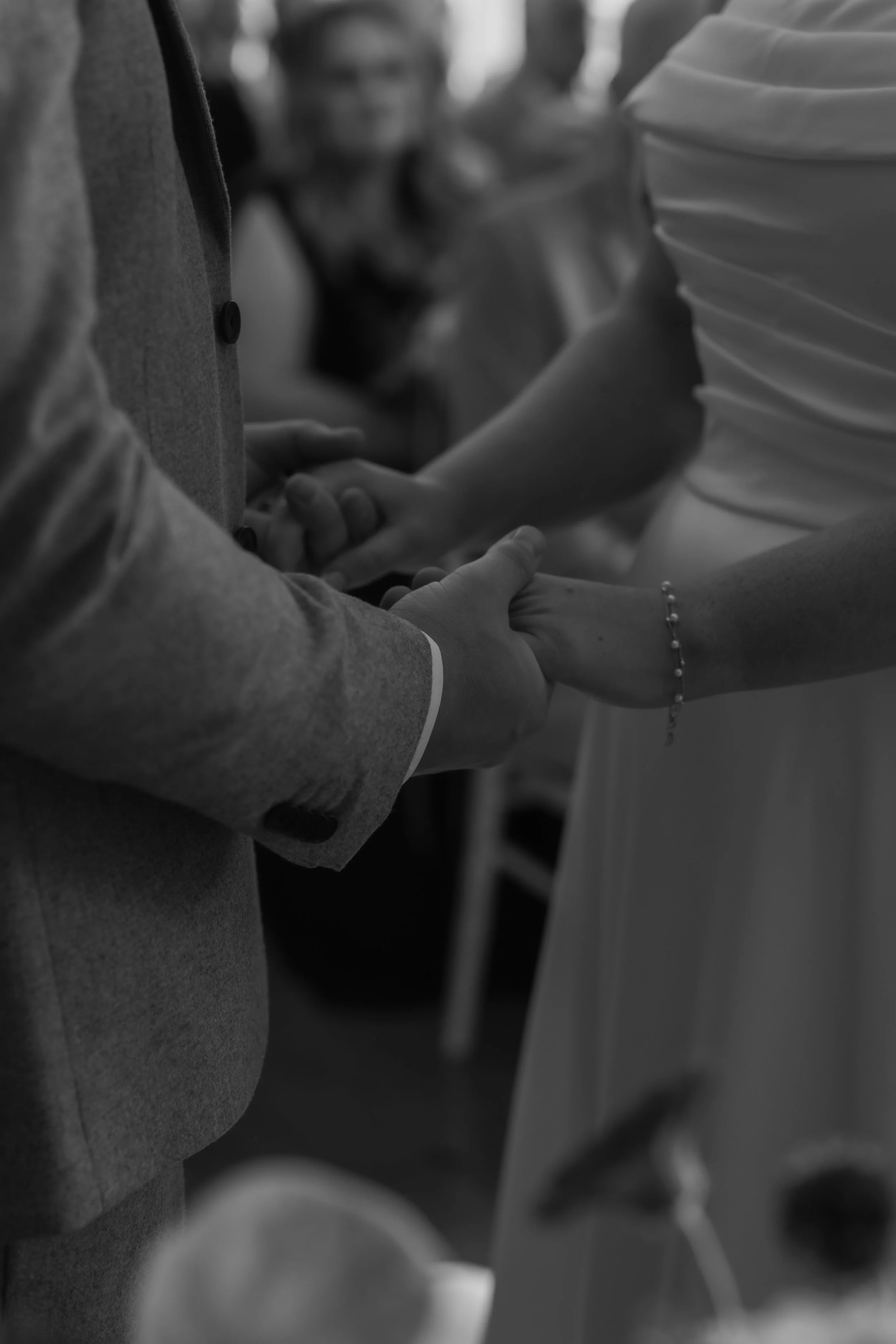 A black and white photo of a couple holding hands during a wedding ceremony, with the bride and groom standing close to each other.