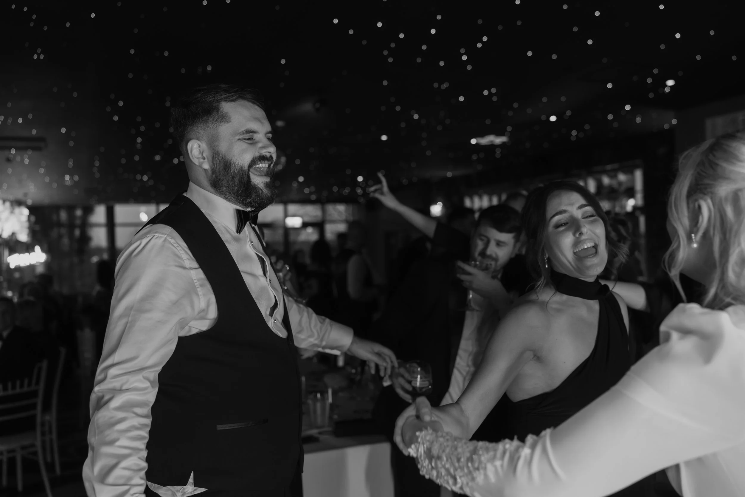 People enjoying a lively celebration indoors, smiling and dancing, with a festive atmosphere and star-like decor on the ceiling.