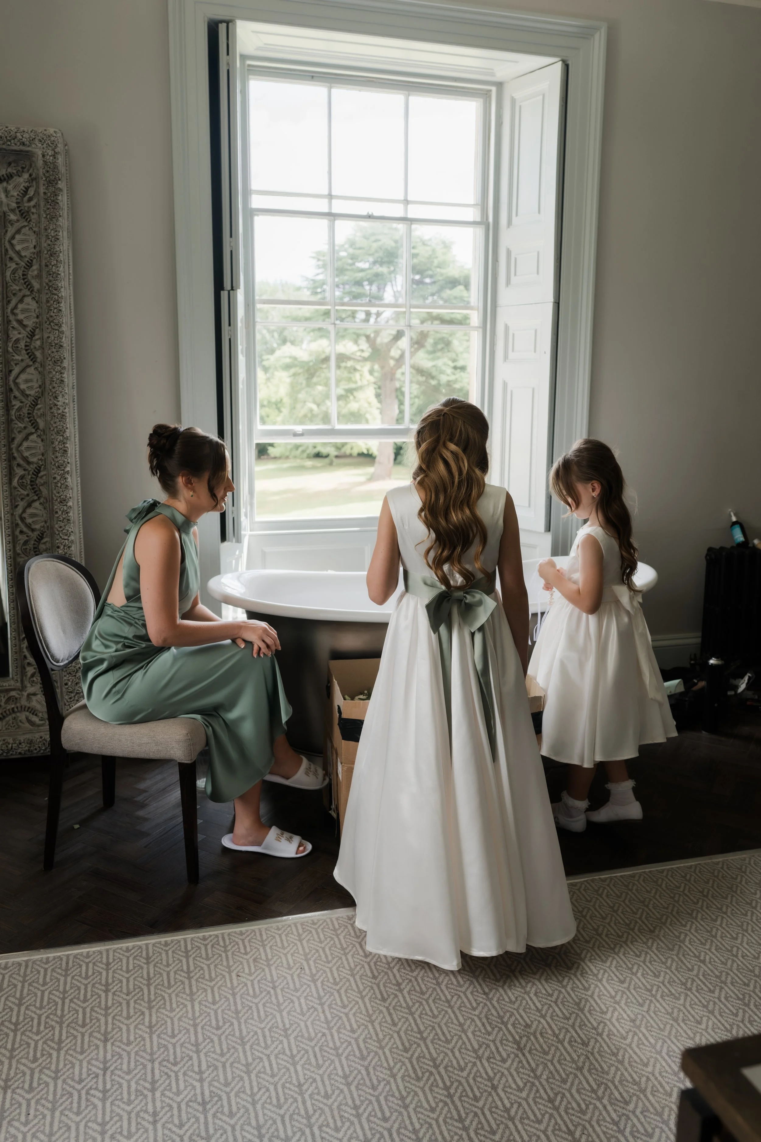 Bridal suit Saltmarshe Hall bridesmaid and flower girls stand around bath tub in front of large window 