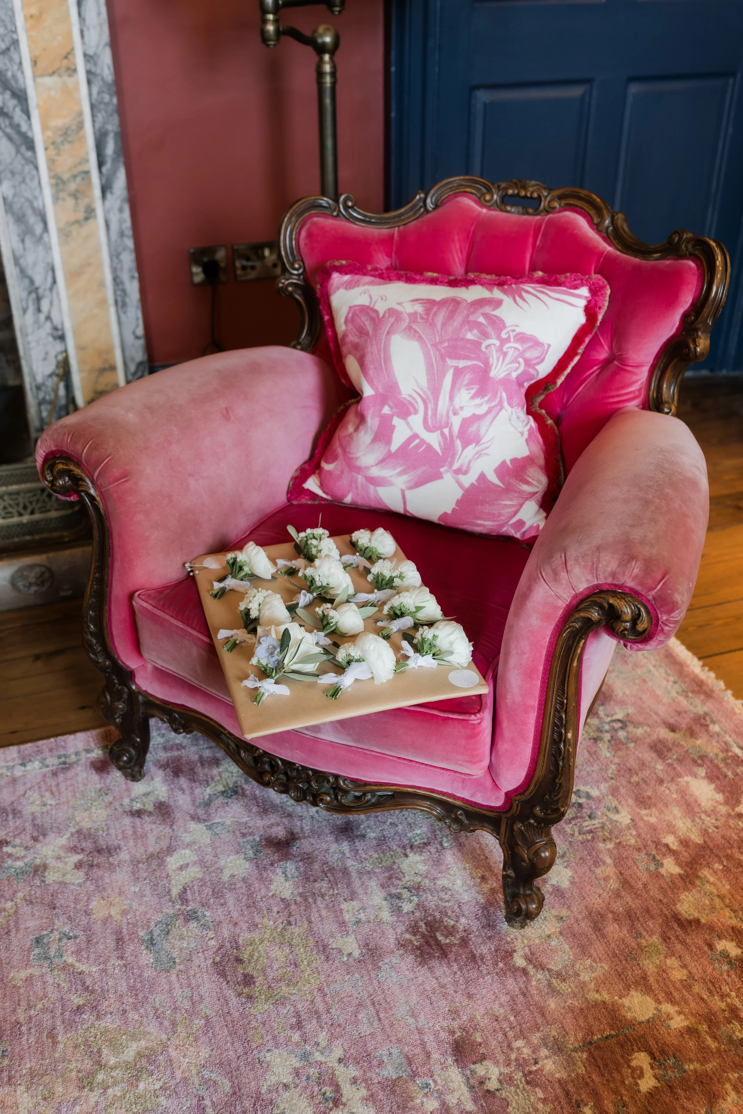 Pink vintage armchair with floral cushion, decorated with a tray of white flowers on the seat.