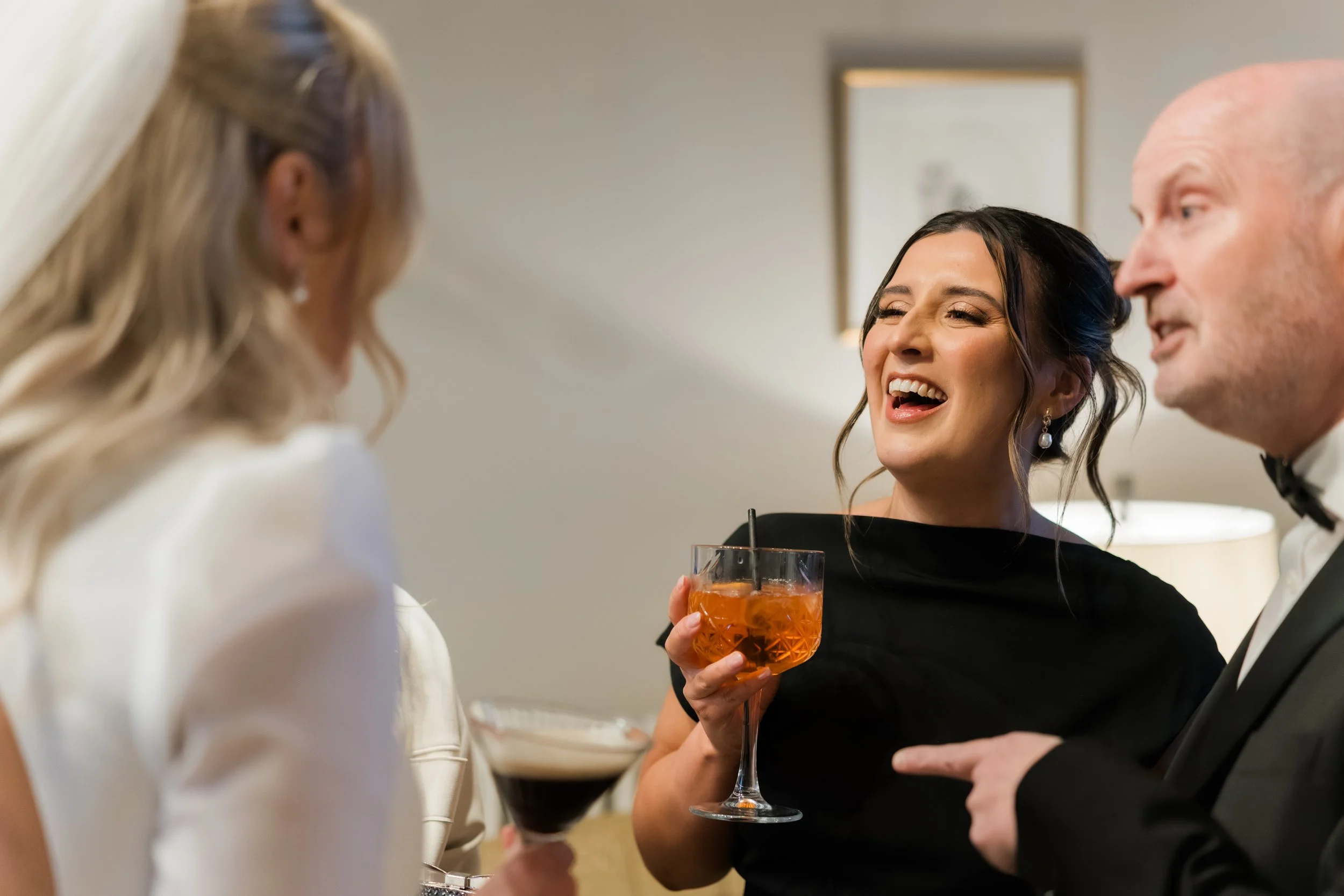 People at a social gathering holding drinks and enjoying conversation, dressed in formal attire.