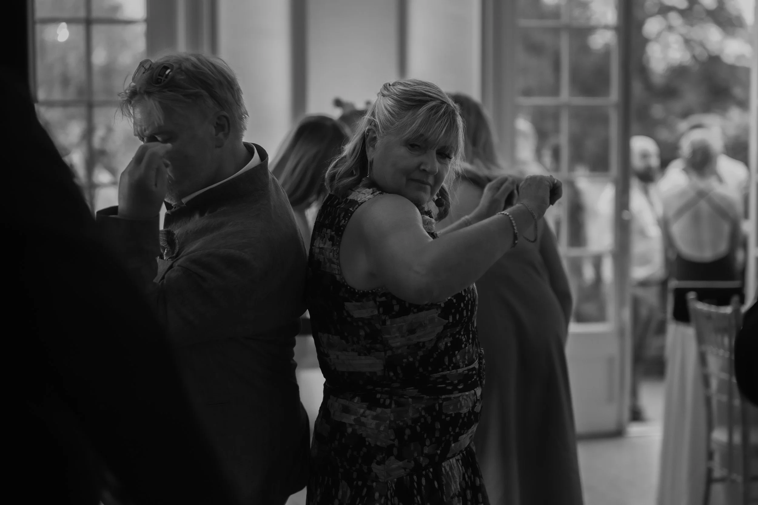 People dancing at a social gathering in a well-lit indoor space with large windows and outdoor scenery in the background.