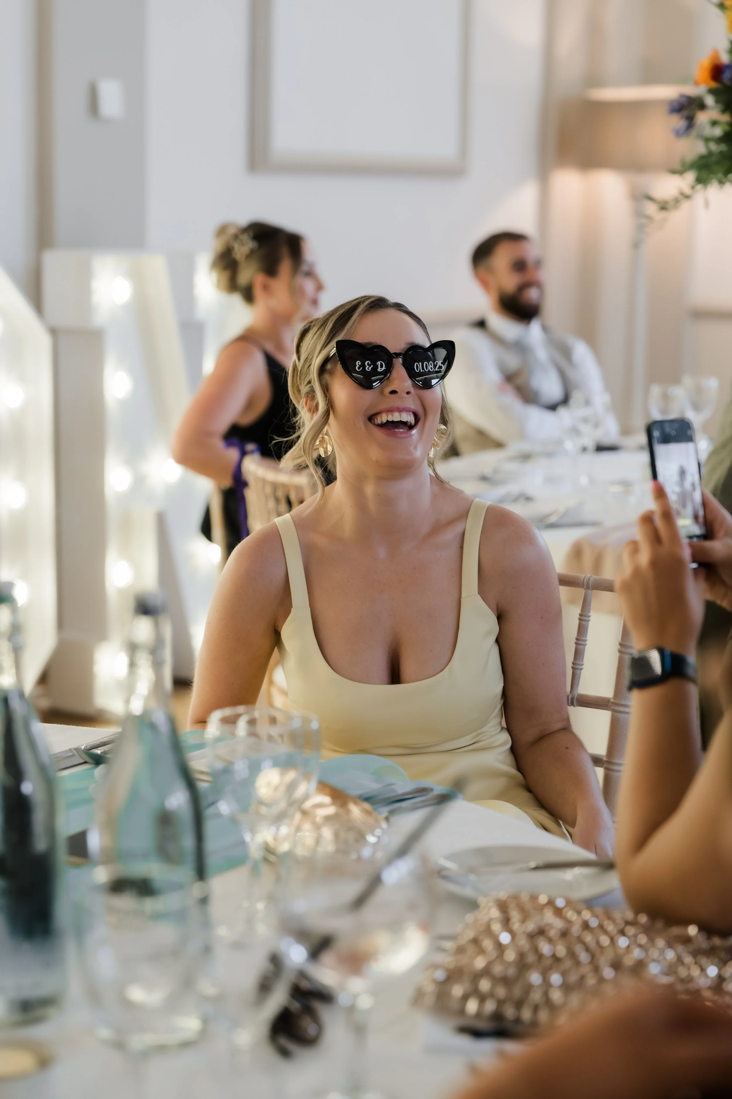 A woman wearing heart-shaped sunglasses with text and a date, smiling and enjoying herself at a celebratory event.